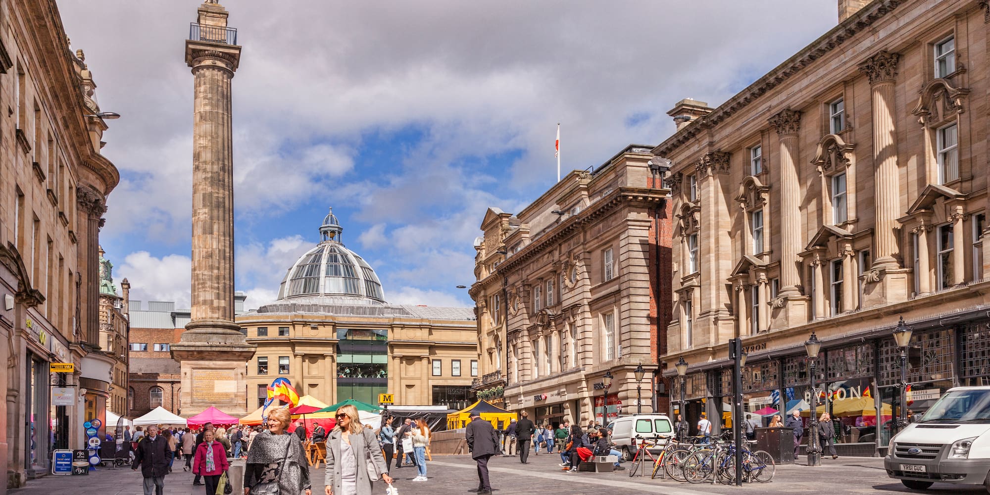 Newcastle city square with Grey's Monument, Grainger Market dome, and market stalls.