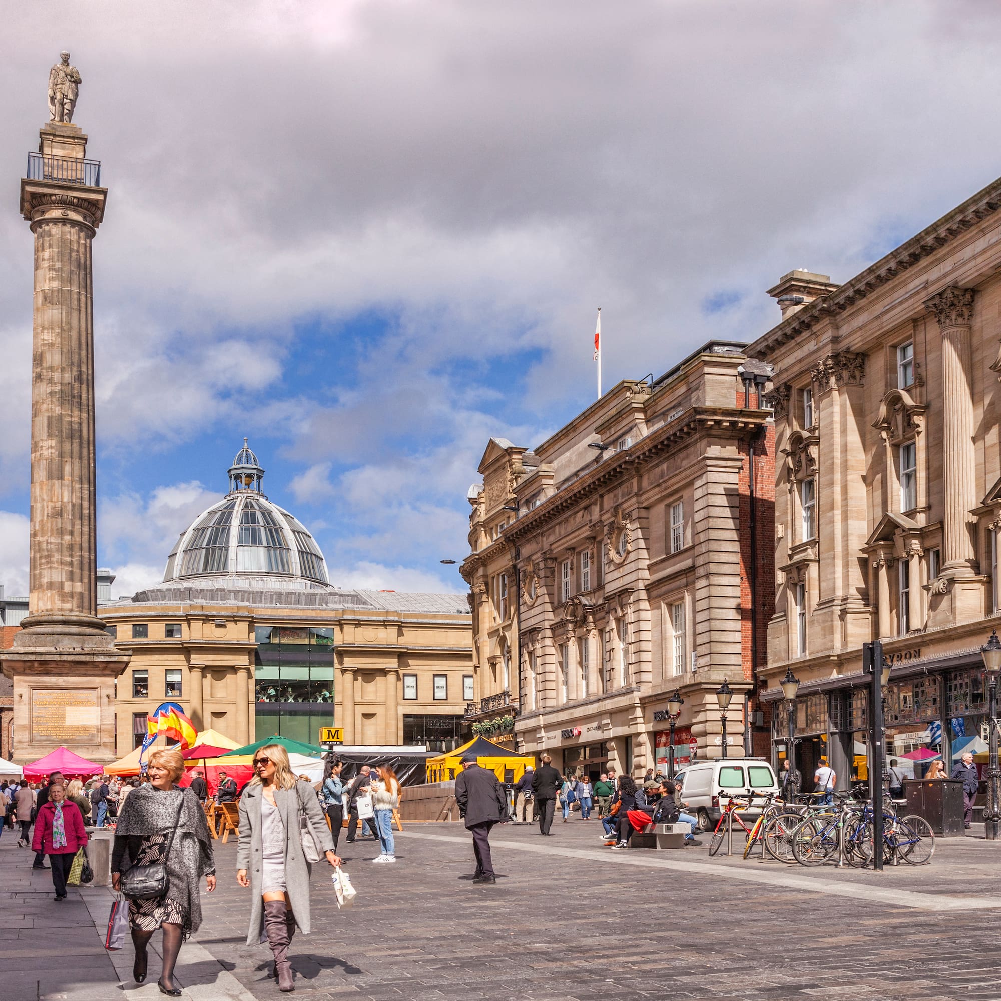 Newcastle city square with Grey's Monument, Grainger Market dome, and market stalls.