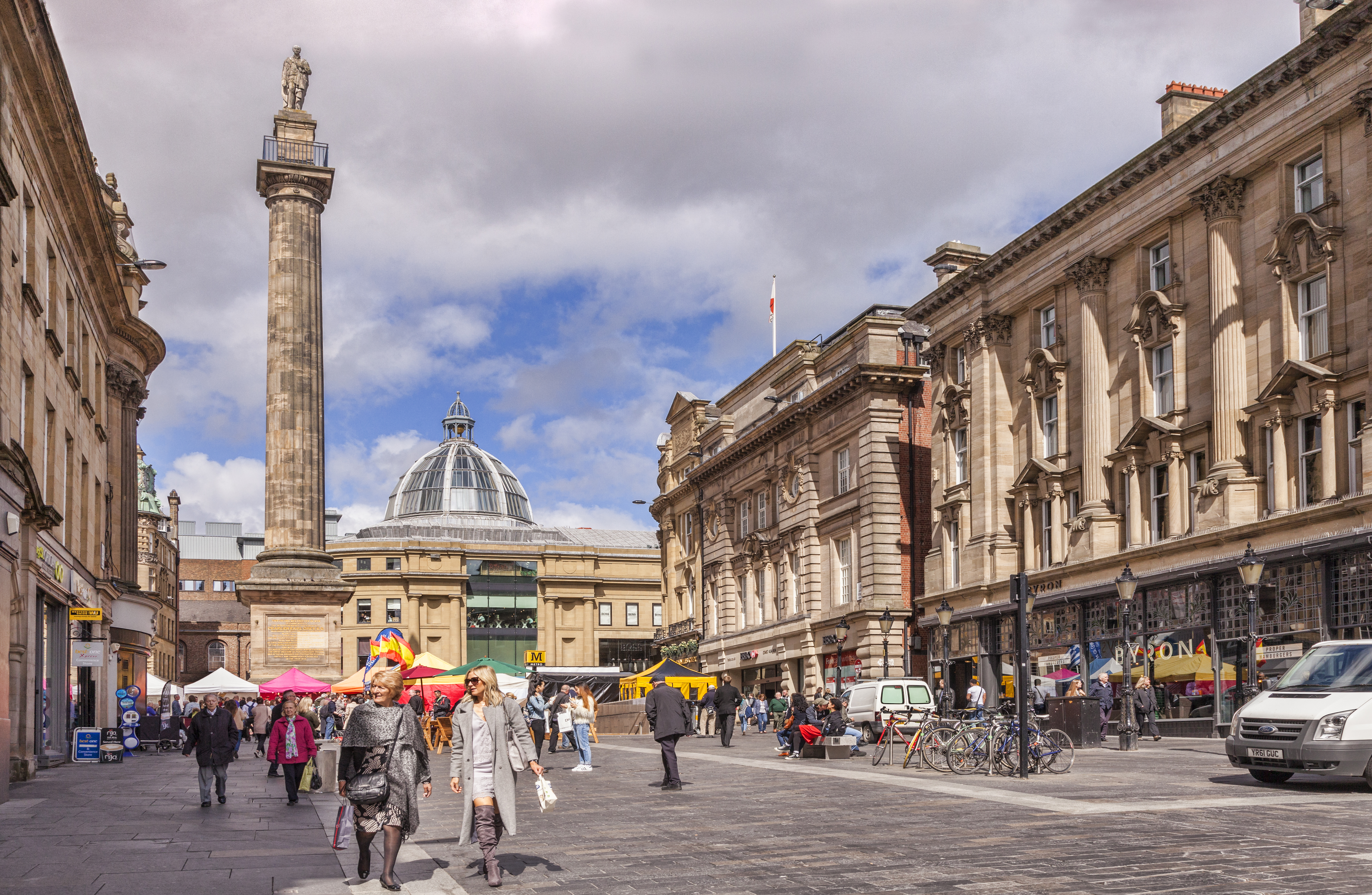 Newcastle city square with Grey's Monument, Grainger Market dome, and market stalls.