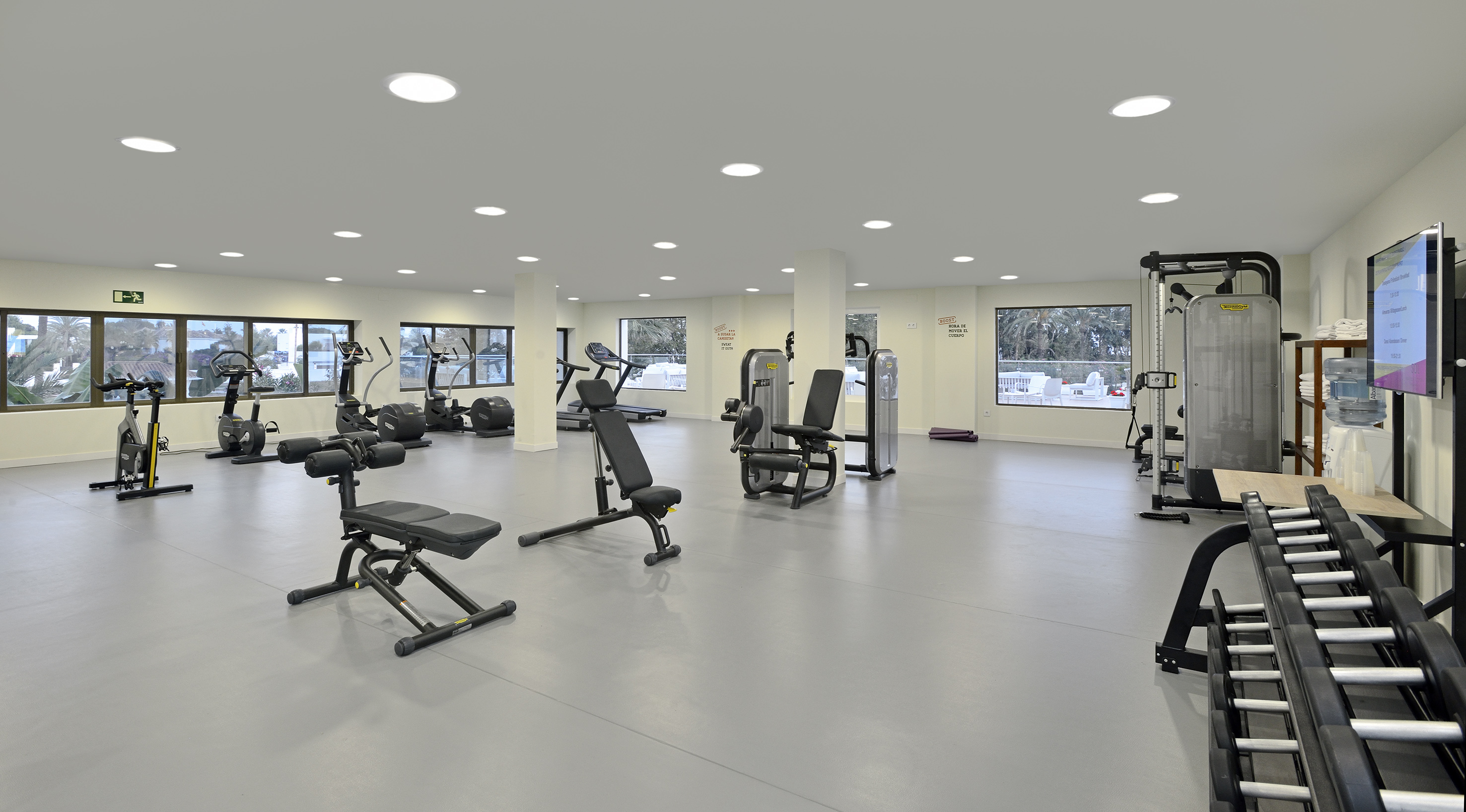 Bright hotel gym featuring cardio machines, strength equipment, and outdoor scenery.