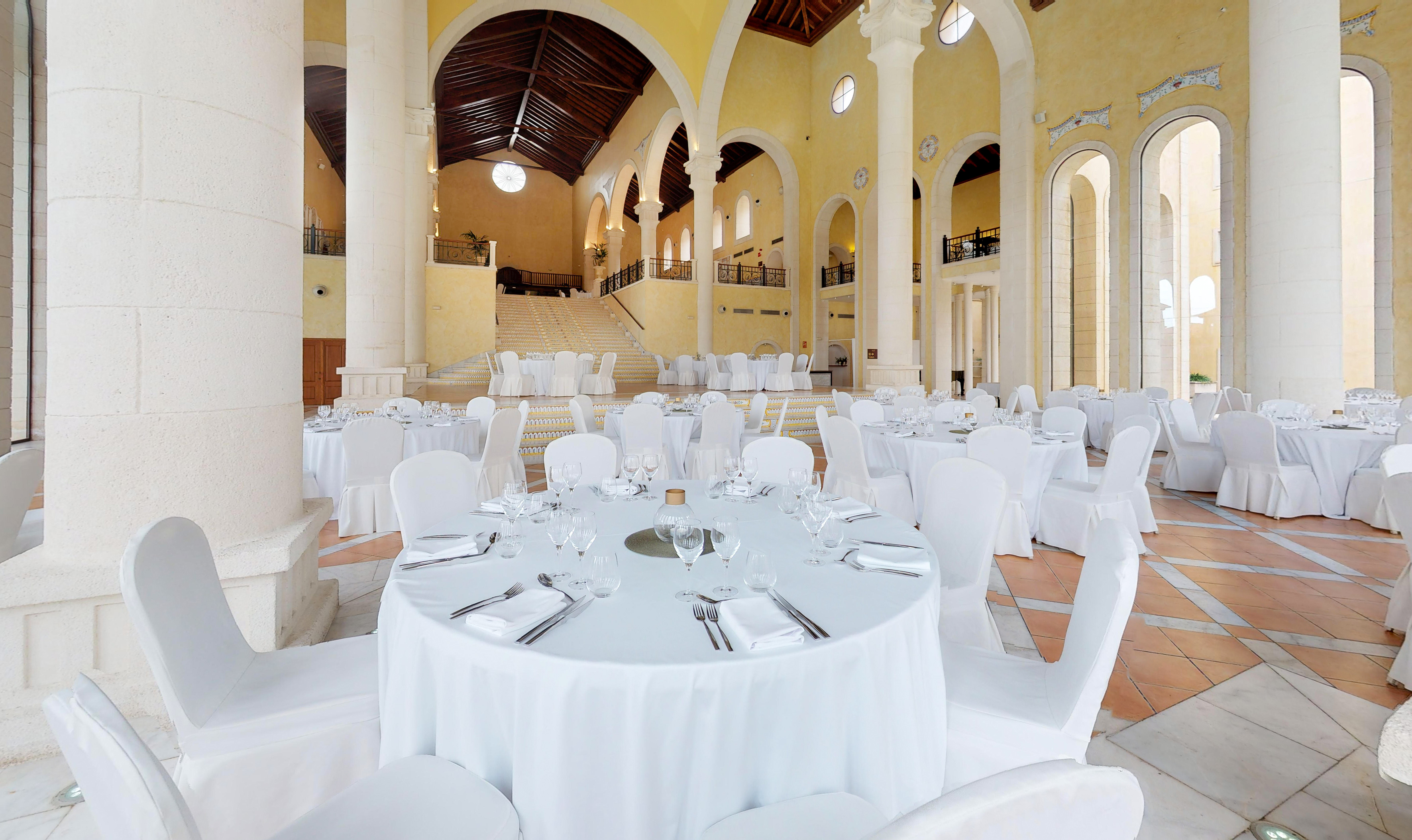Elegant event hall with white banquet tables, grand architecture, and high ceilings.