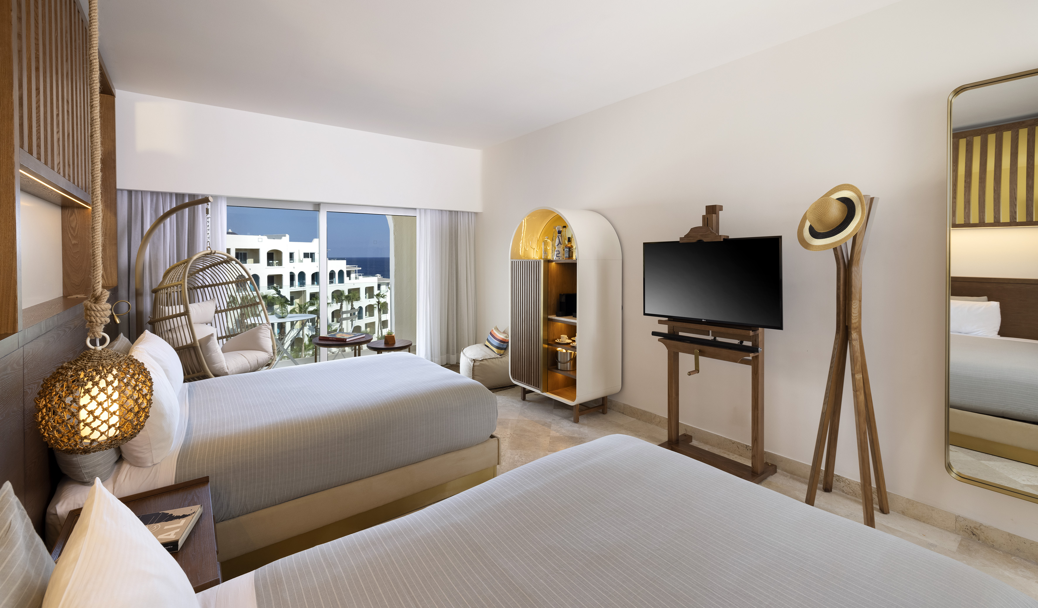 Coastal hotel room with two beds, ocean view balcony, and hanging chair.