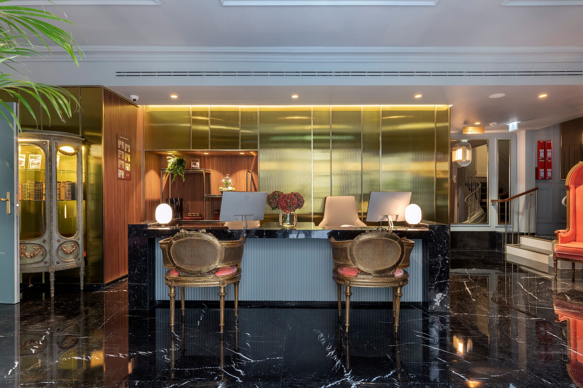 Luxury hotel reception desk with black marble, gold wall, computers, and elegant chairs.