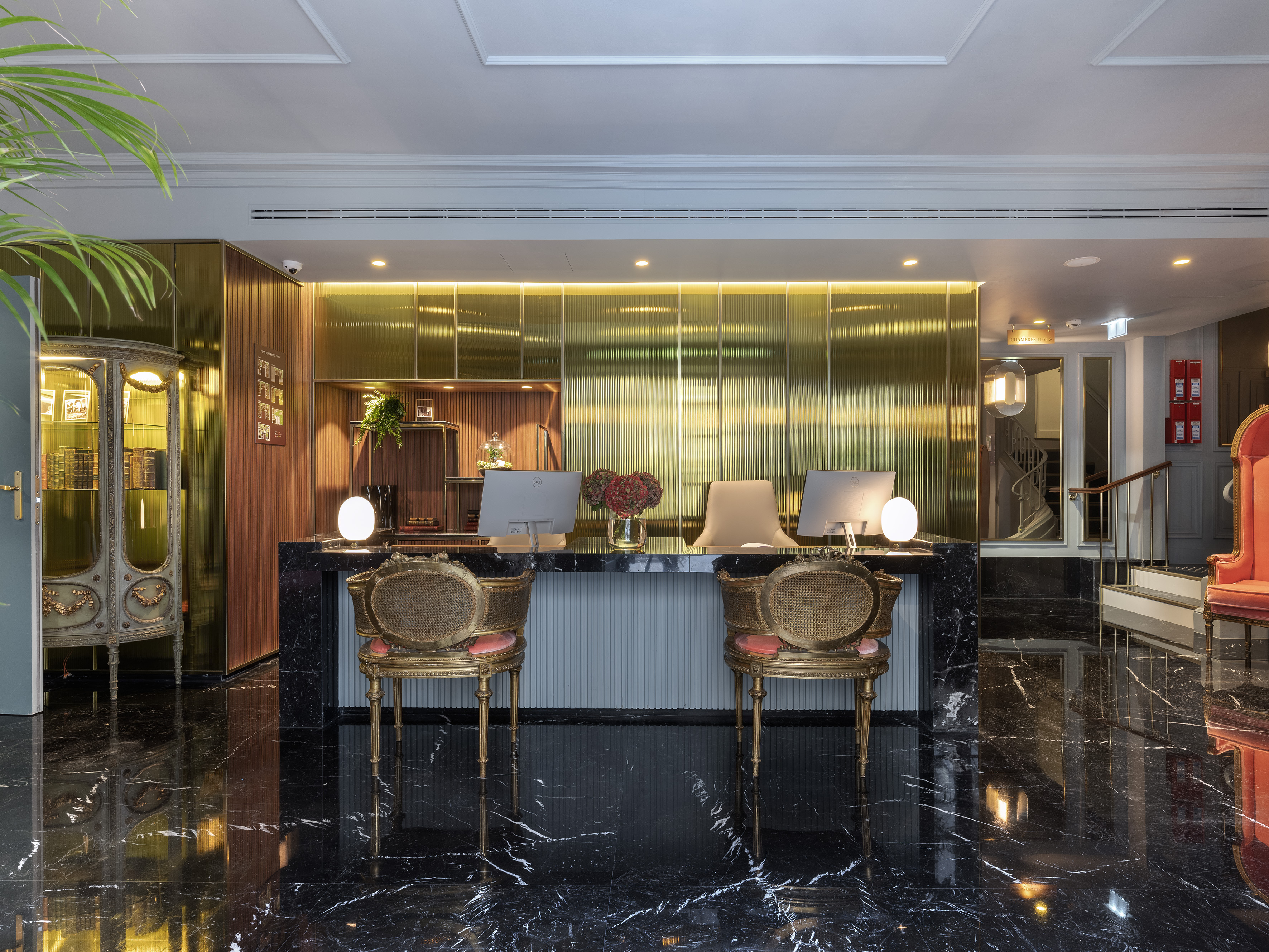 Luxury hotel reception desk with black marble, gold wall, computers, and elegant chairs.