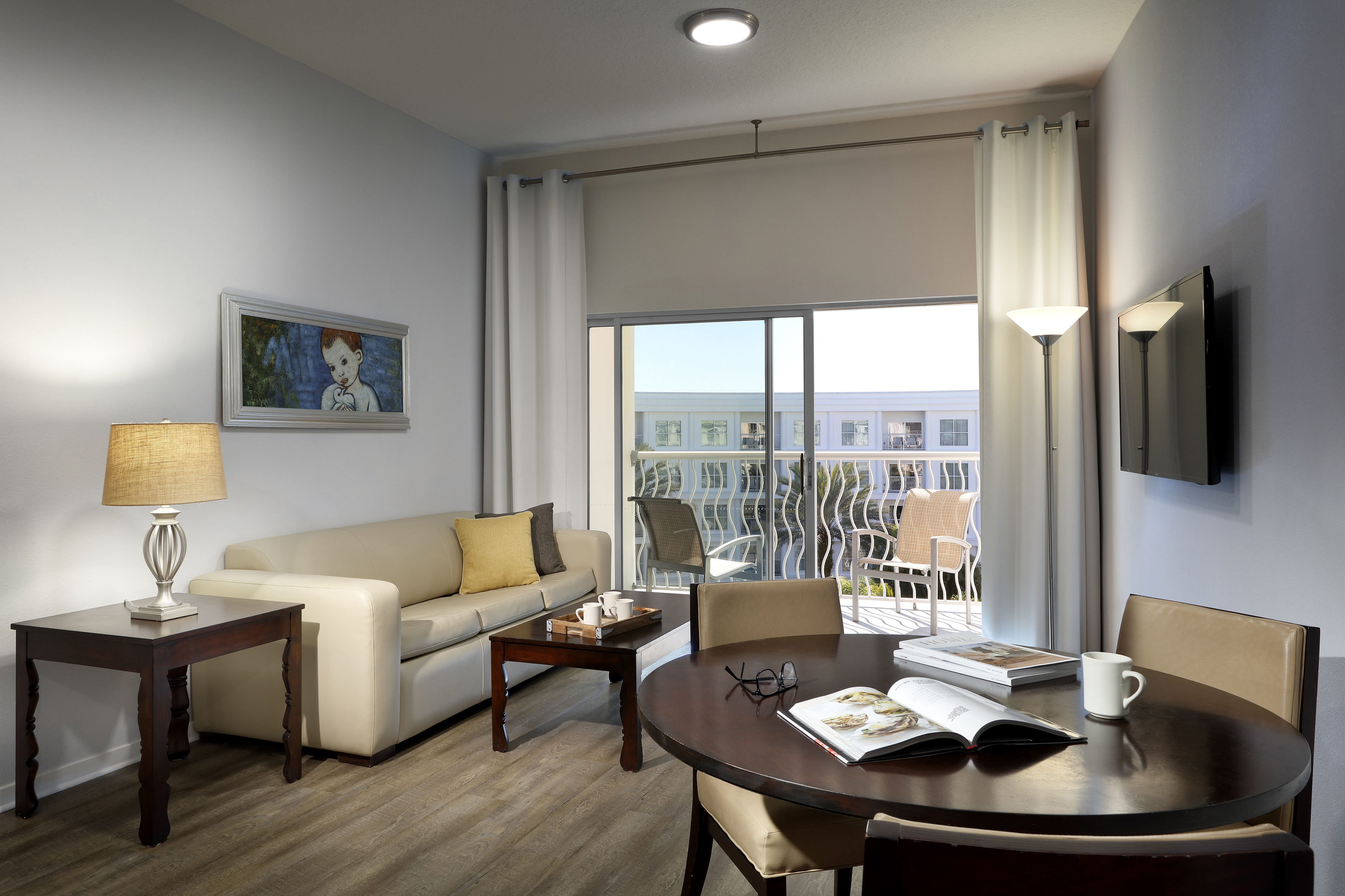 Living and dining area with sofa, round dining table, and balcony access. - Two-Bedroom Suite - Meliá Orlando Celebration, Orlando