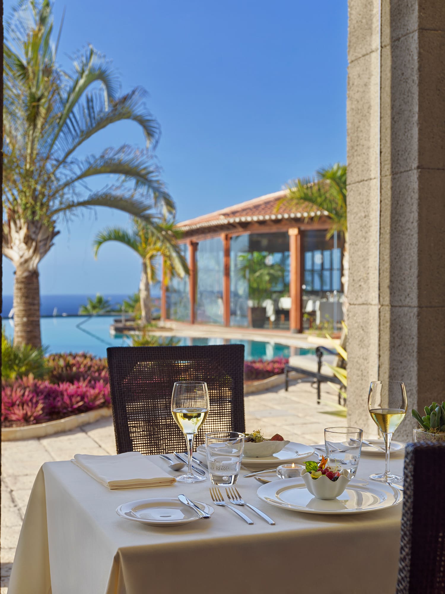 a table set for a meal outside with a pool and palm trees