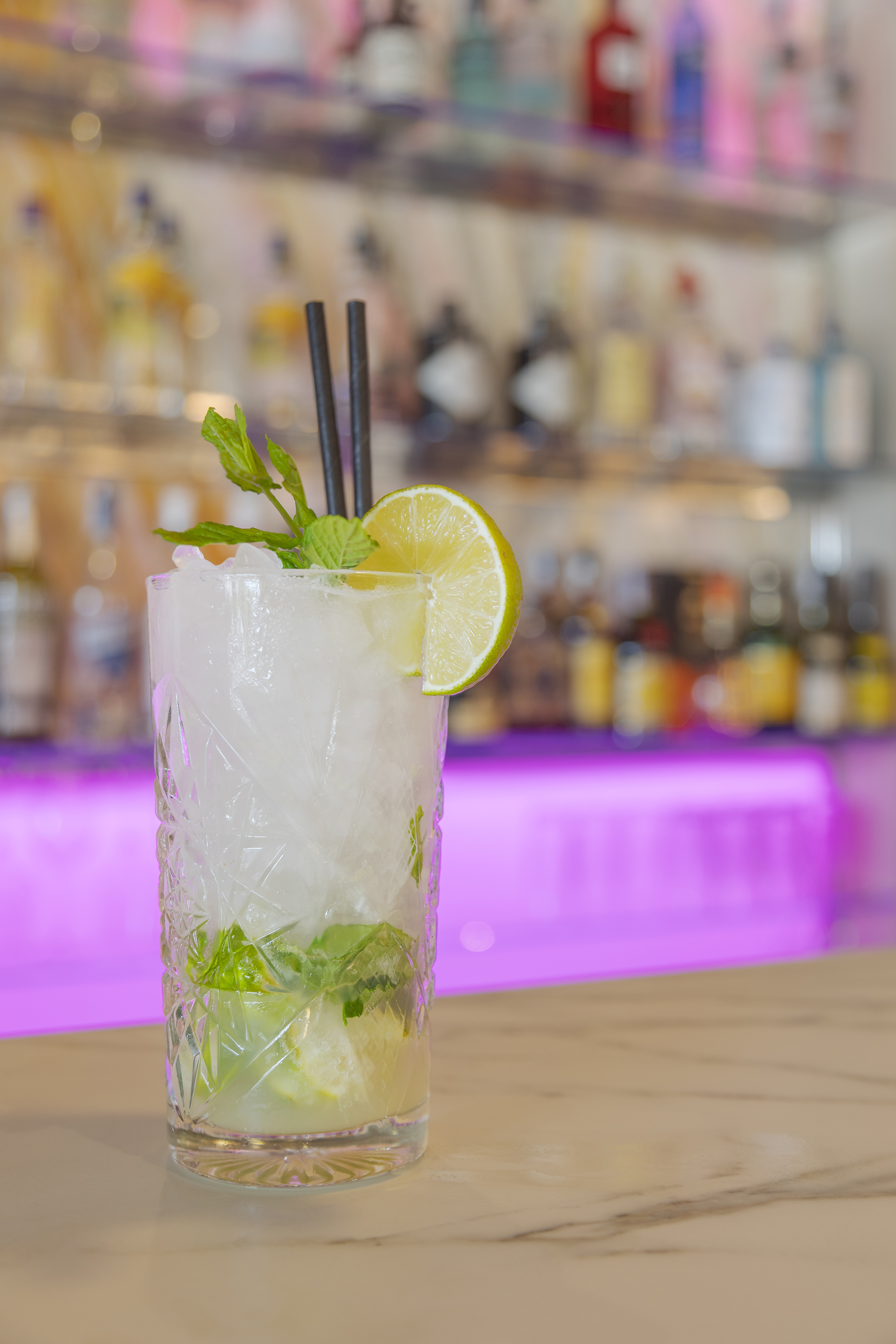 Mojito cocktail with mint, lime, and ice on a bar counter with blurred bottles.
