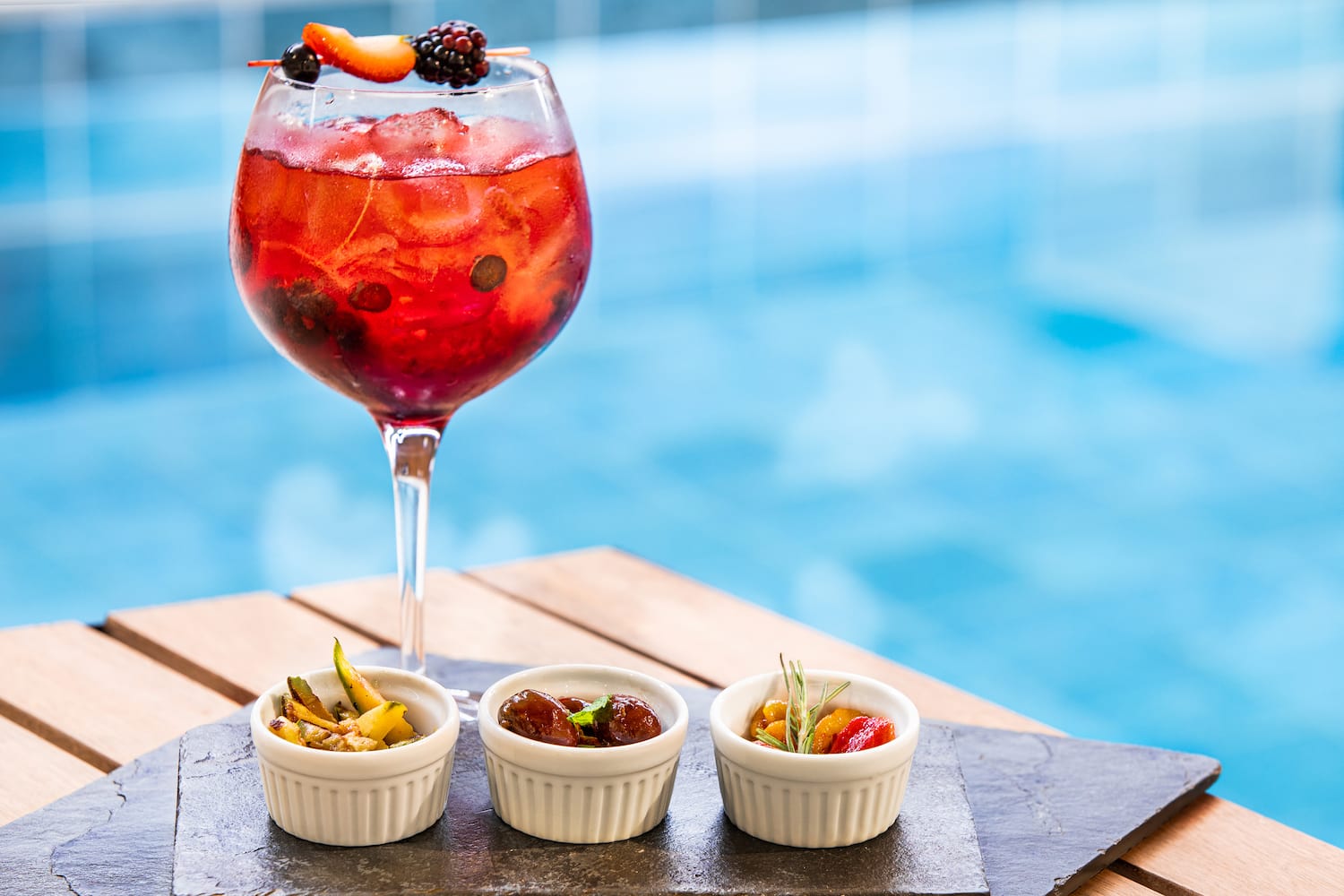 a glass of red liquid with fruit in front of small white bowls of fruit