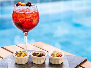 a glass of red liquid with fruit in front of small white bowls of fruit