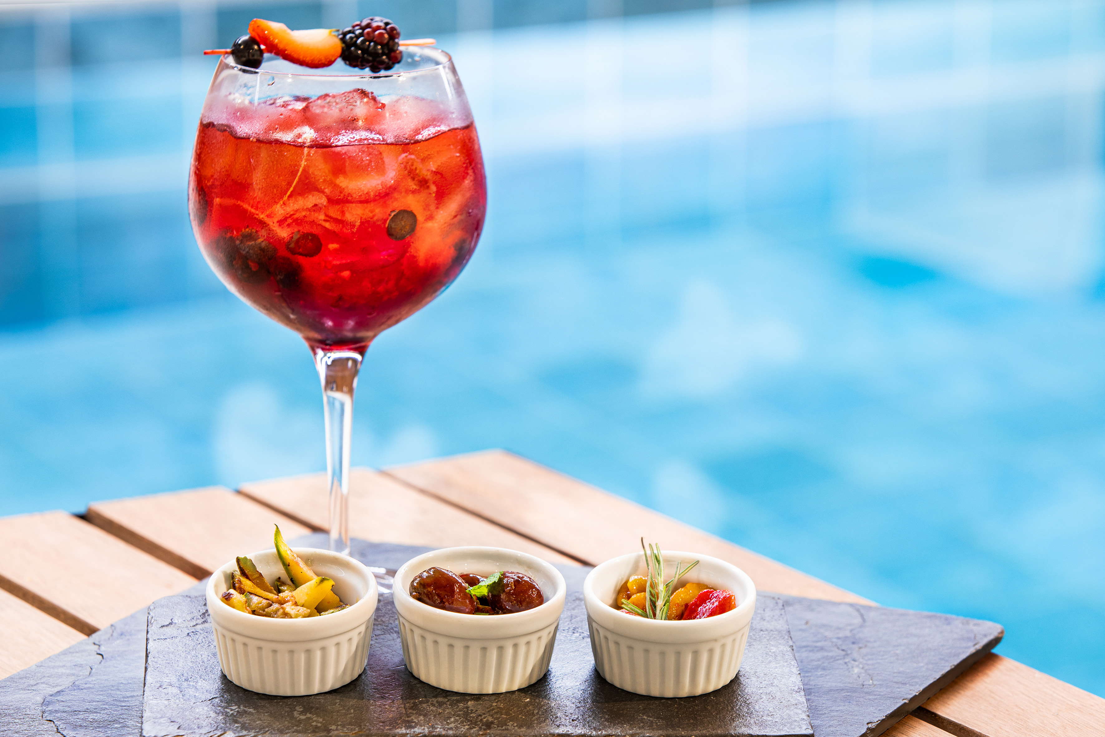 Poolside red berry cocktail and assorted tapas on a slate board.