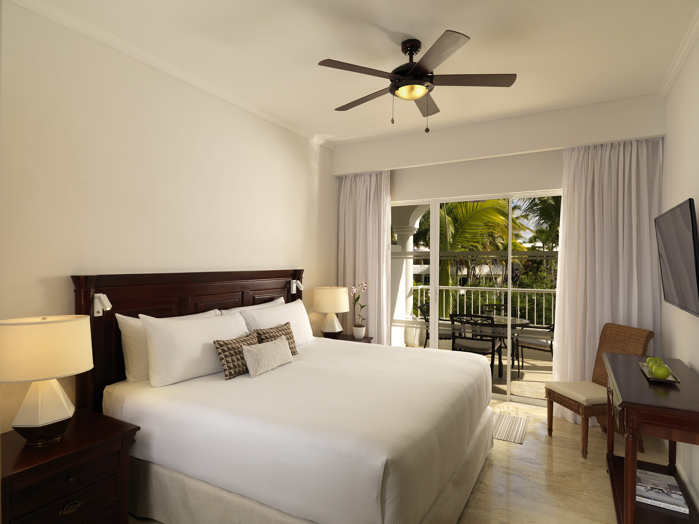 Luxury hotel bedroom with king bed, ceiling fan, and tropical balcony view.