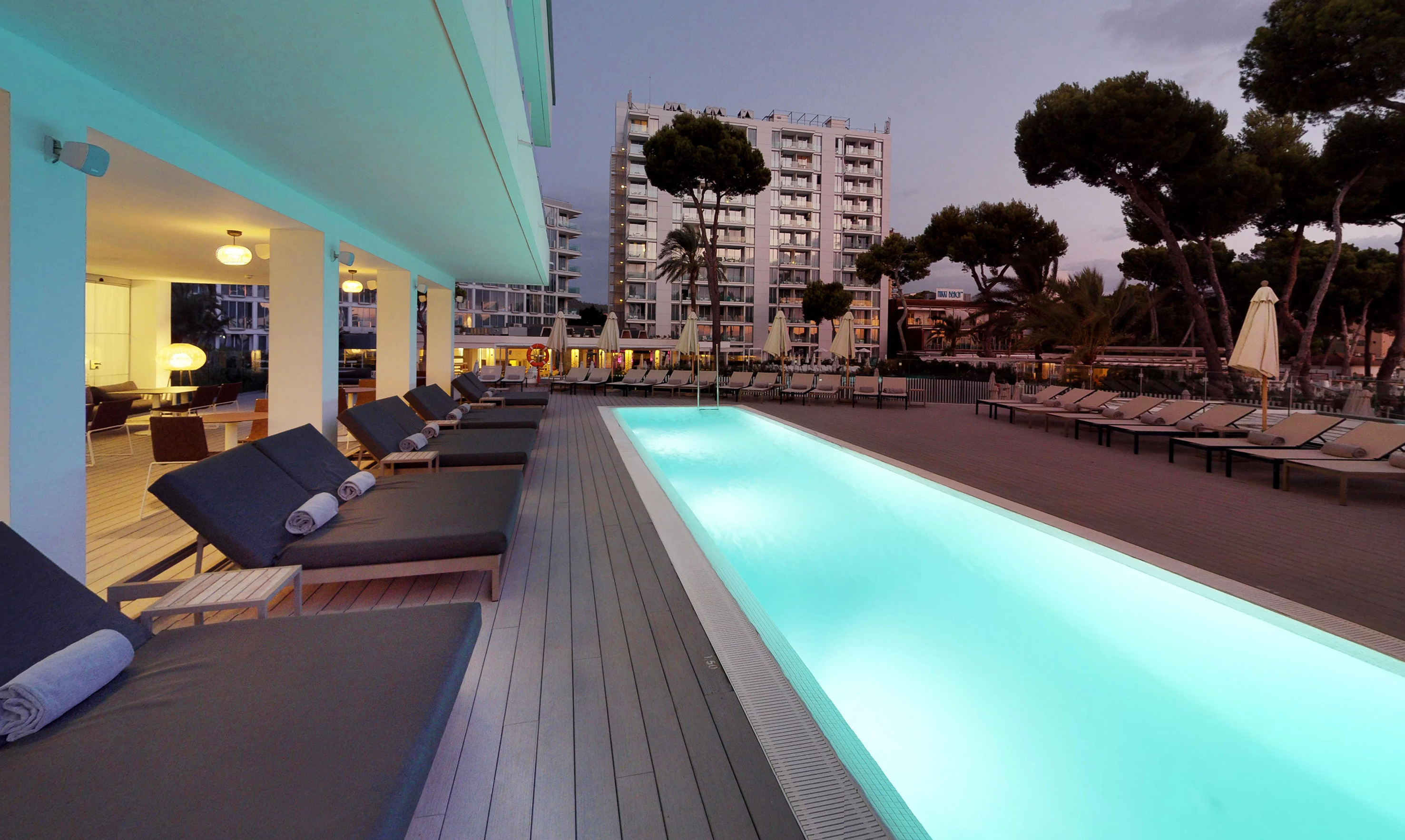Resort swimming pool with lounge chairs at dusk, illuminated blue water.