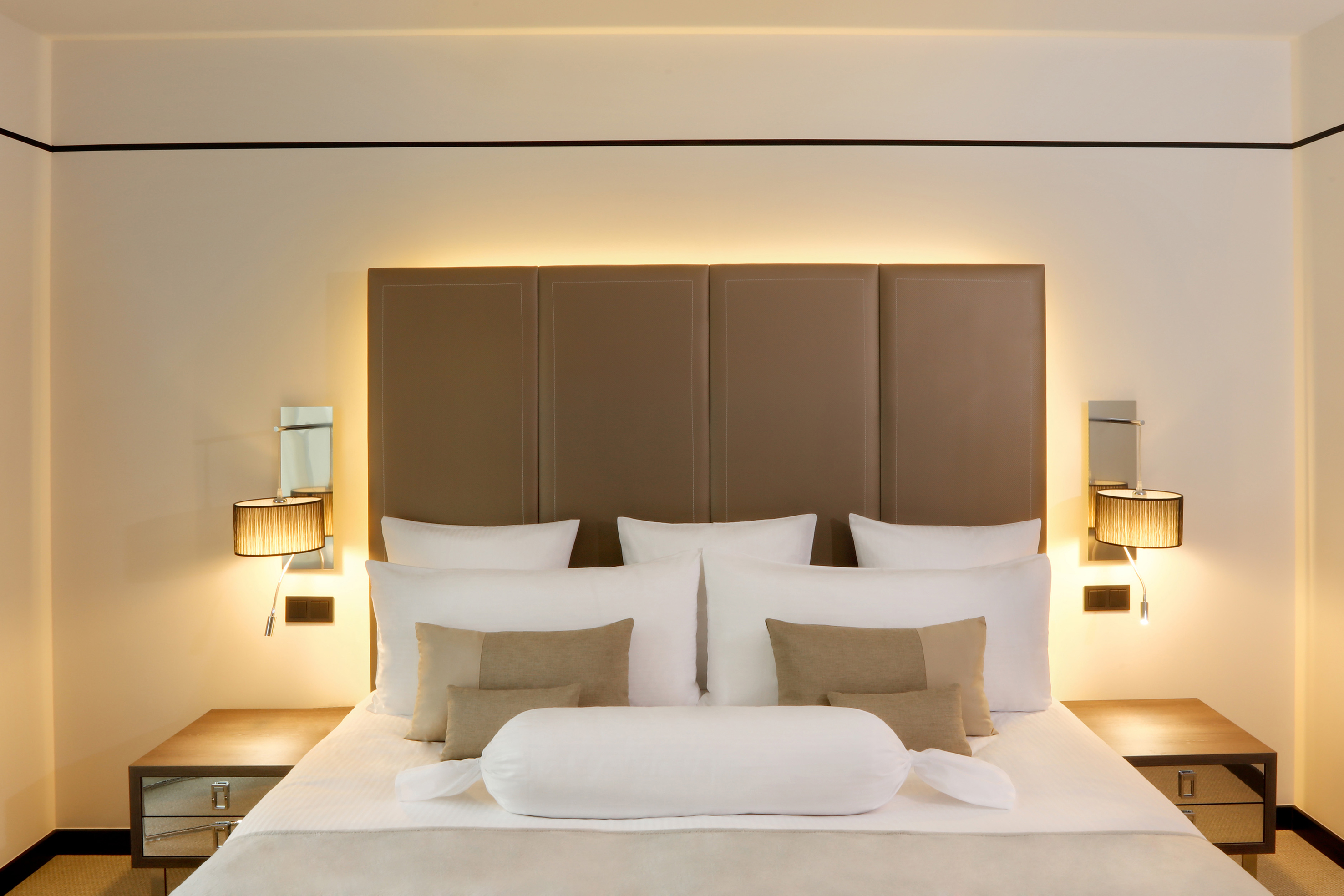 Modern hotel room with cozy bed, upholstered headboard, and warm ambient lighting.