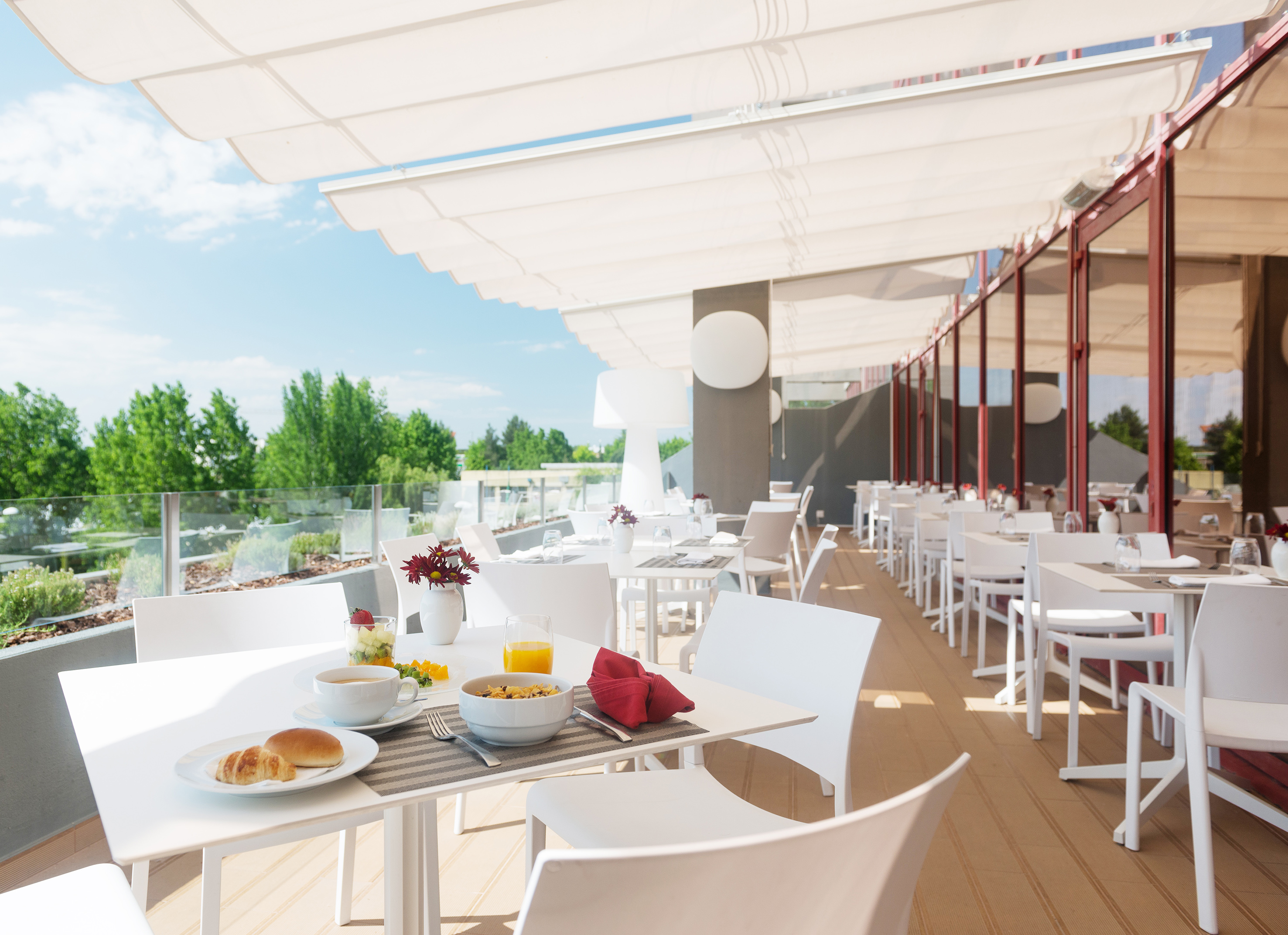 Sunny hotel terrace with breakfast on white tables and a large canopy.