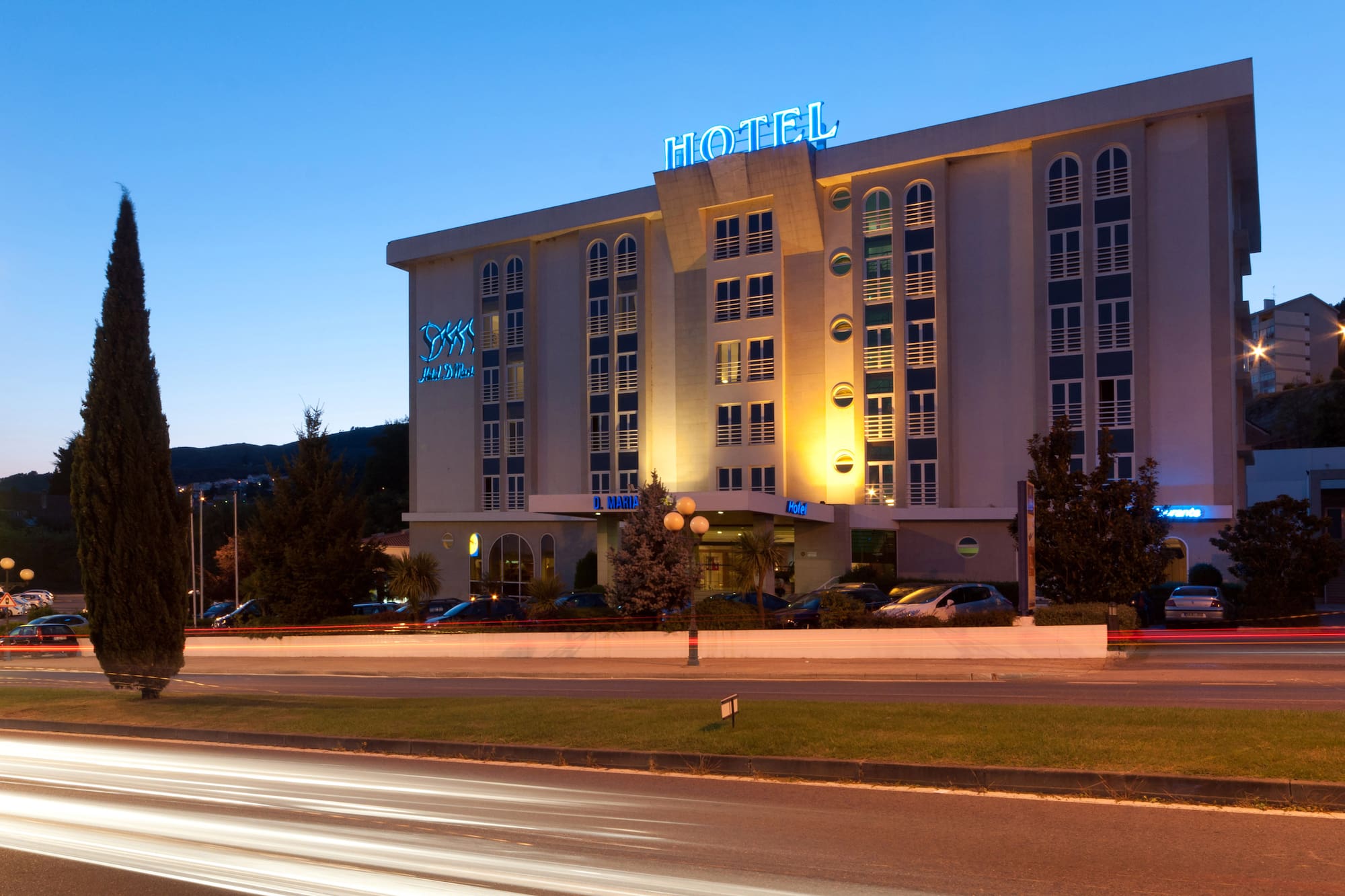 Hotel building at dusk with blue neon signs and traffic light trails.