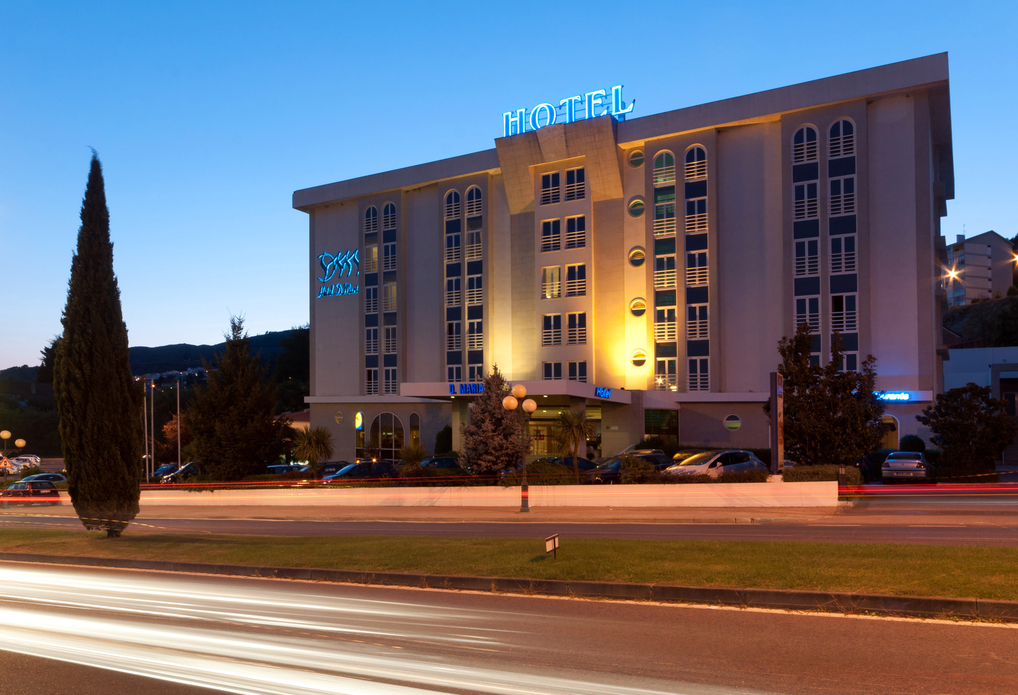 Hotel building at dusk with blue neon signs and traffic light trails.