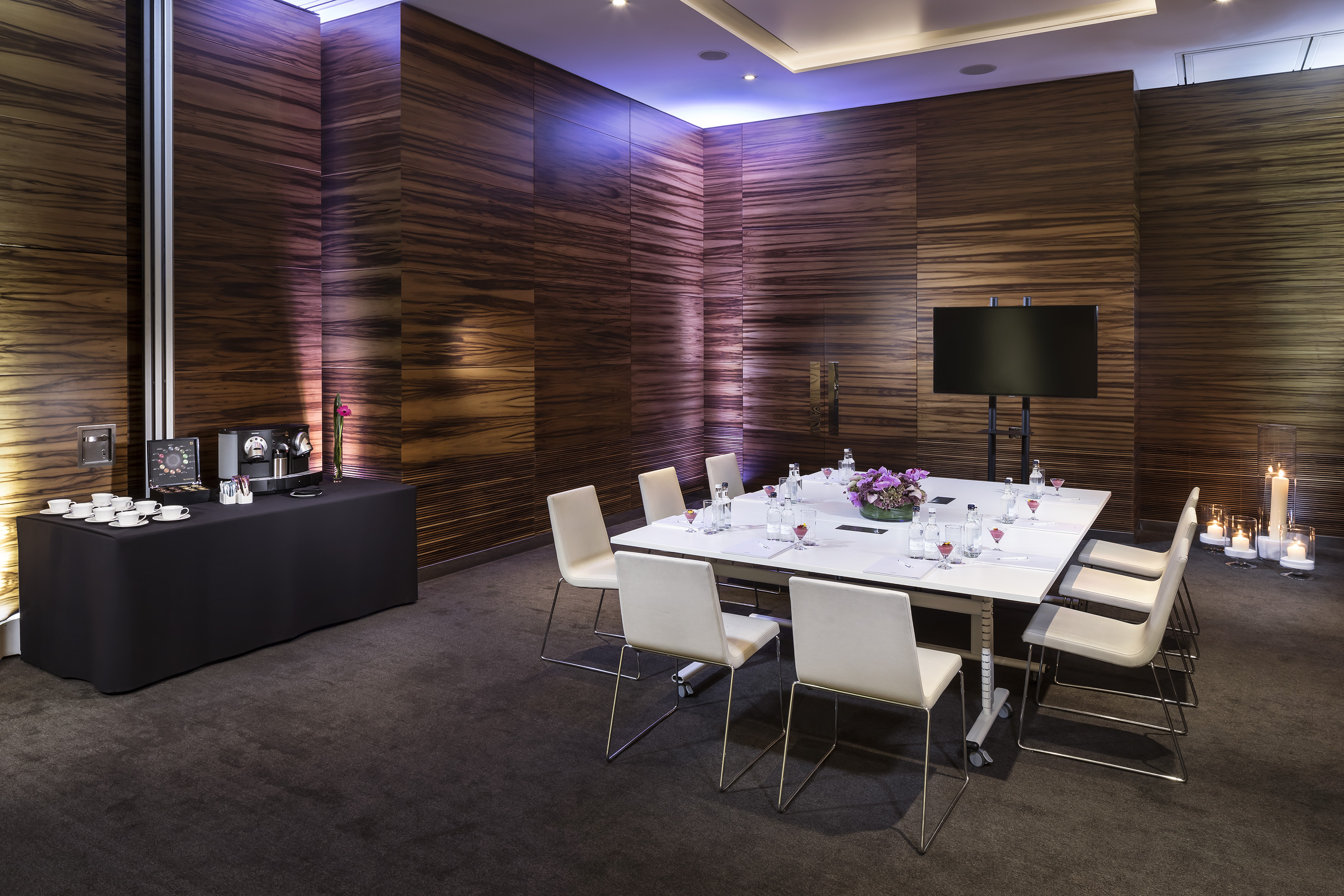 Wood-paneled meeting room with conference table, TV, and coffee station.