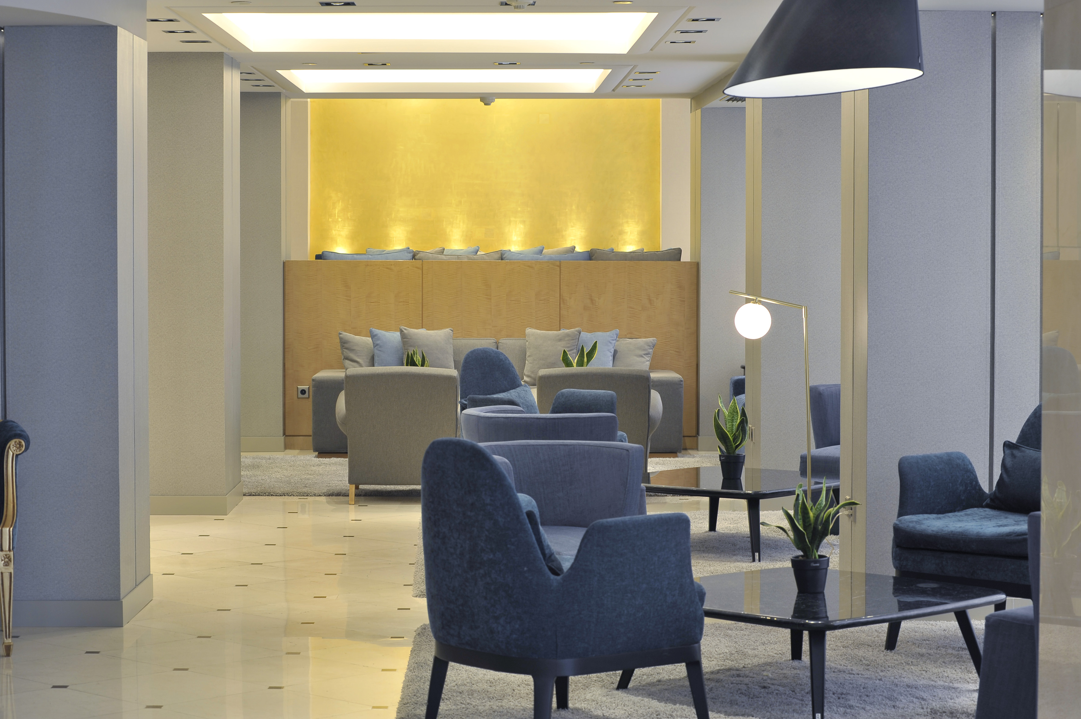 Modern hotel lobby lounge with blue armchairs, grey sofas, and gold accent wall.