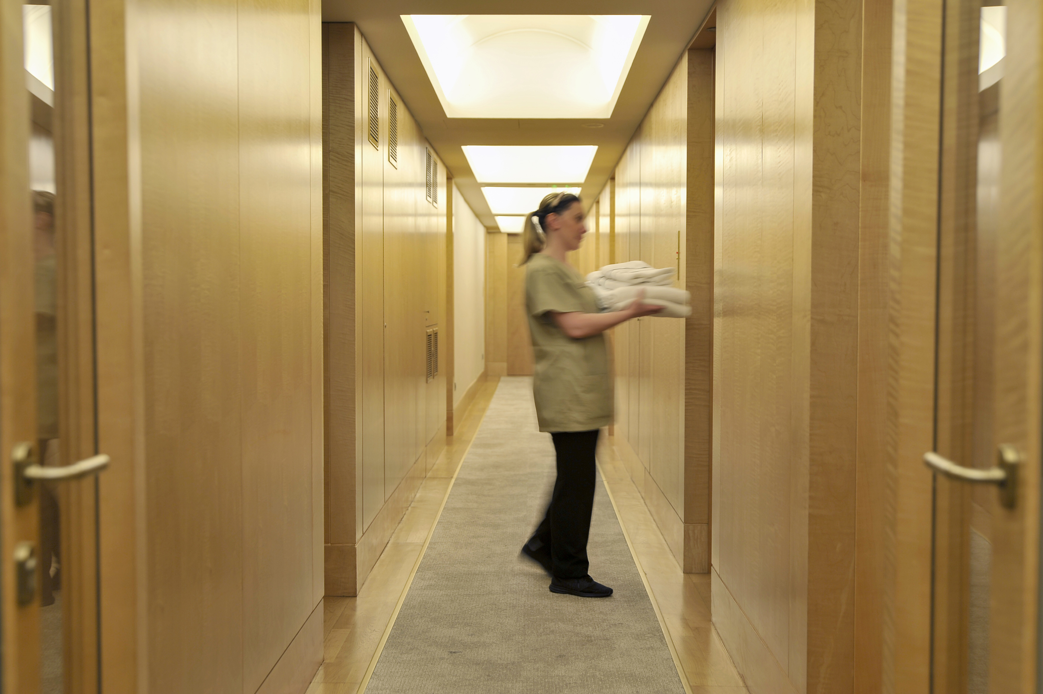 Hotel housekeeper carries fresh towels in a wood-paneled hallway.
