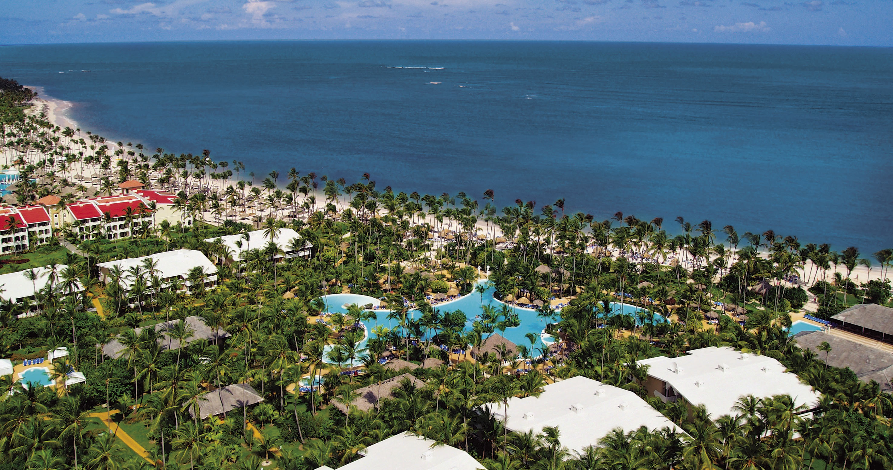 Aerial view tropical beach resort with palm trees, pools, and blue ocean.