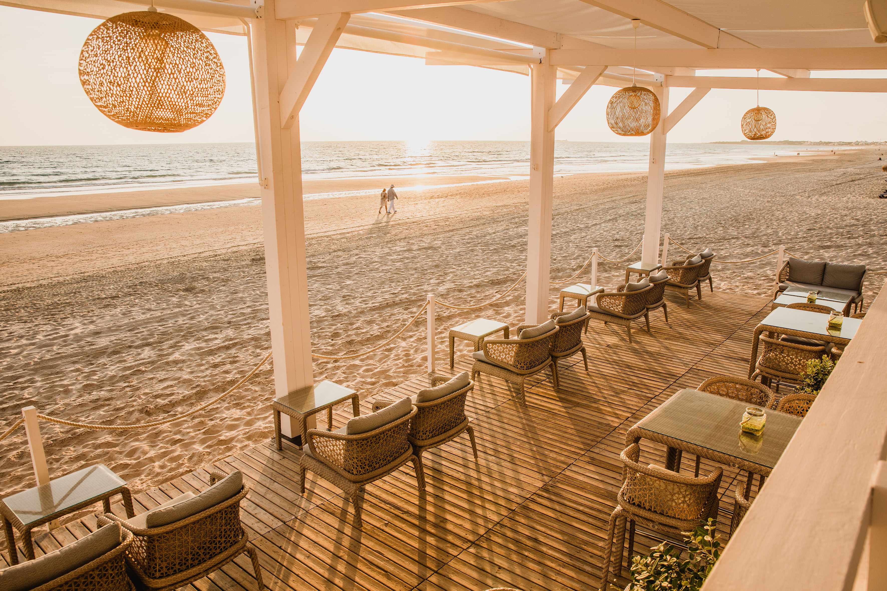 Beach restaurant patio with wicker furniture overlooking the ocean at sunset.