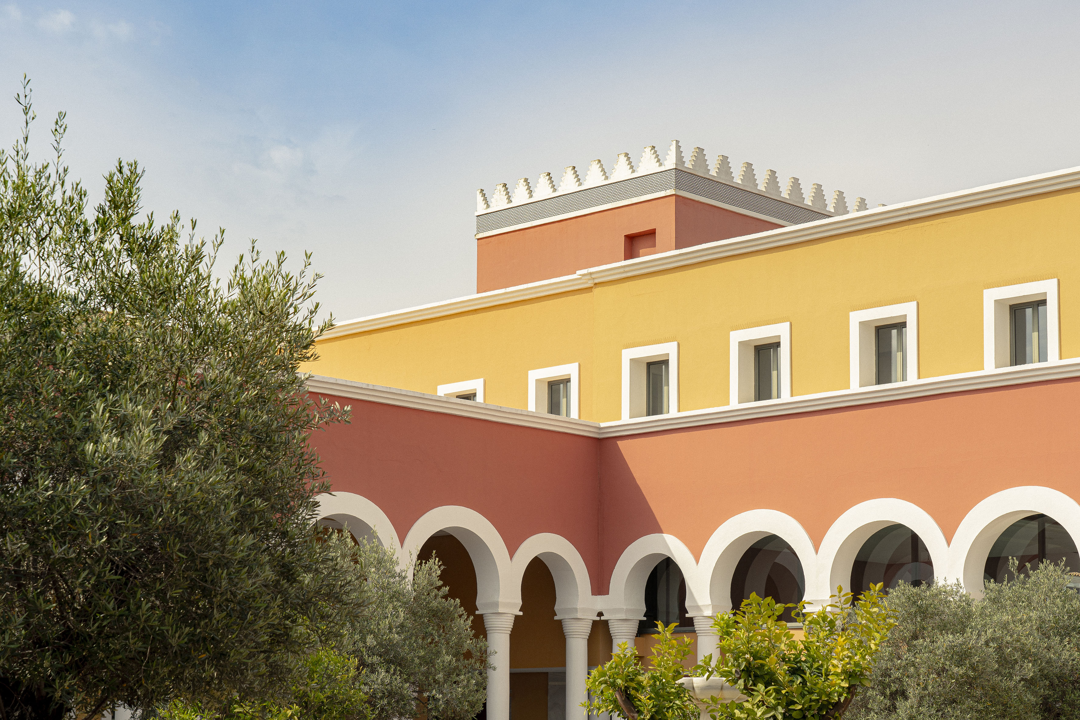 Colorful Mediterranean building with arches, white windows, and olive trees.