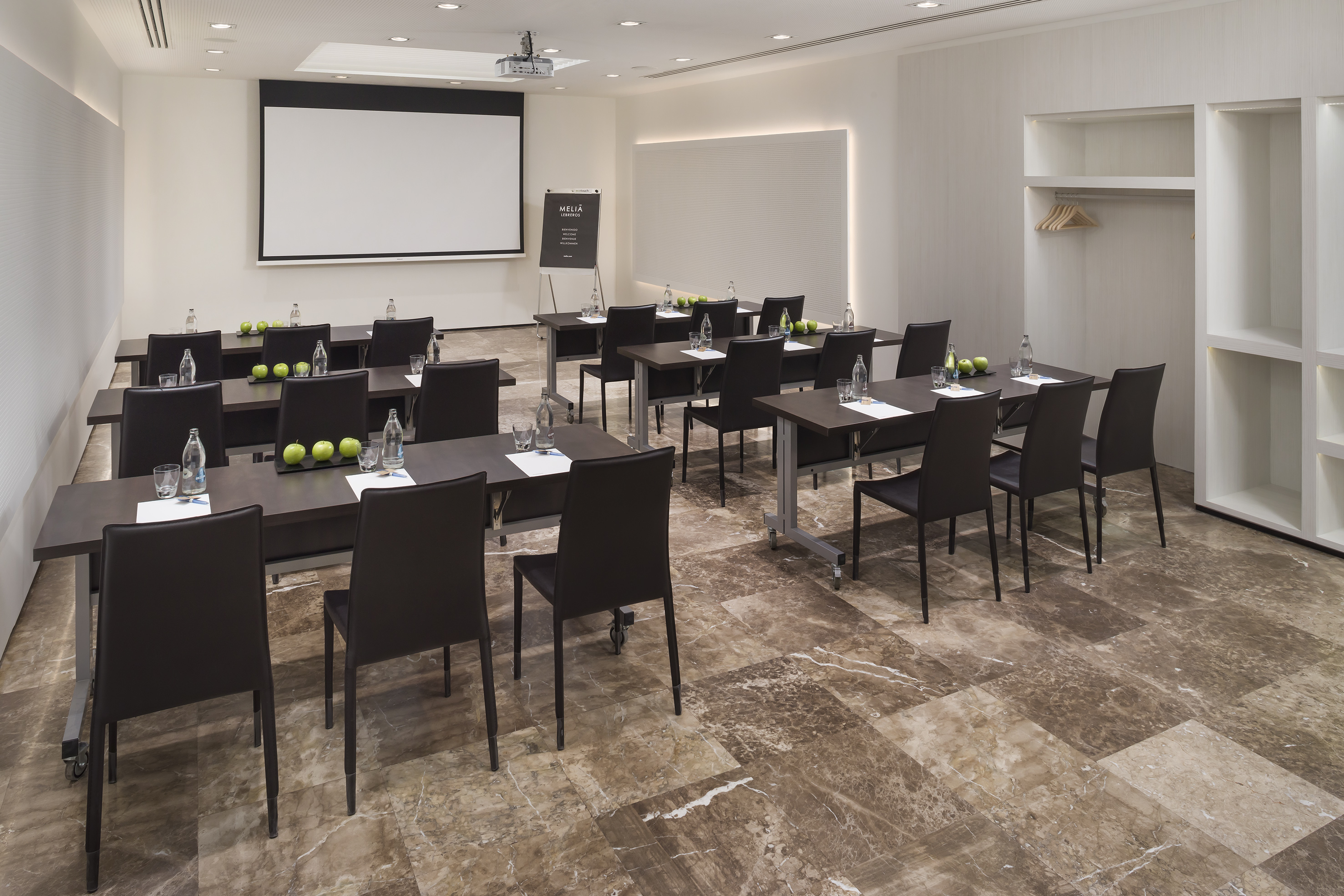 Modern Meliá meeting room with projector screen, tables, chairs, and fresh apples.