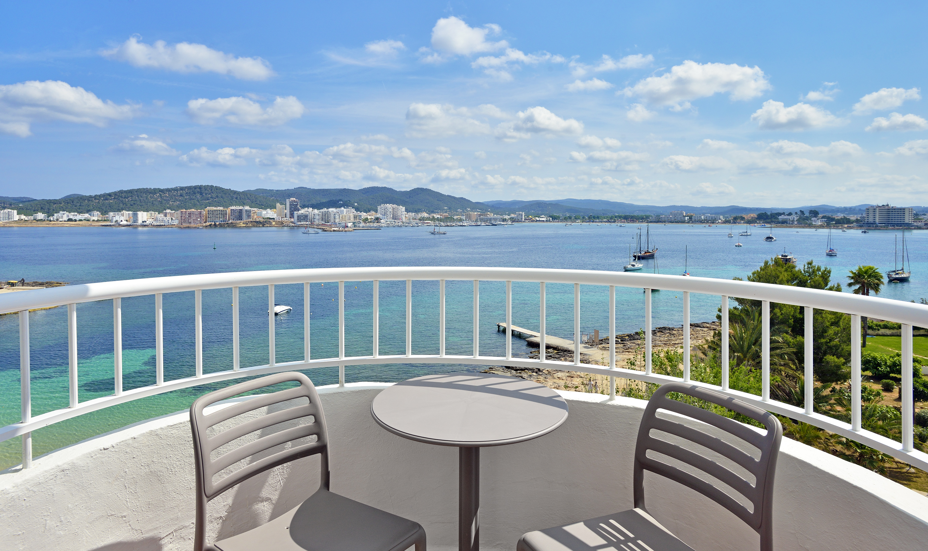 Panoramic balcony view of a sunny bay with boats and a coastal city.