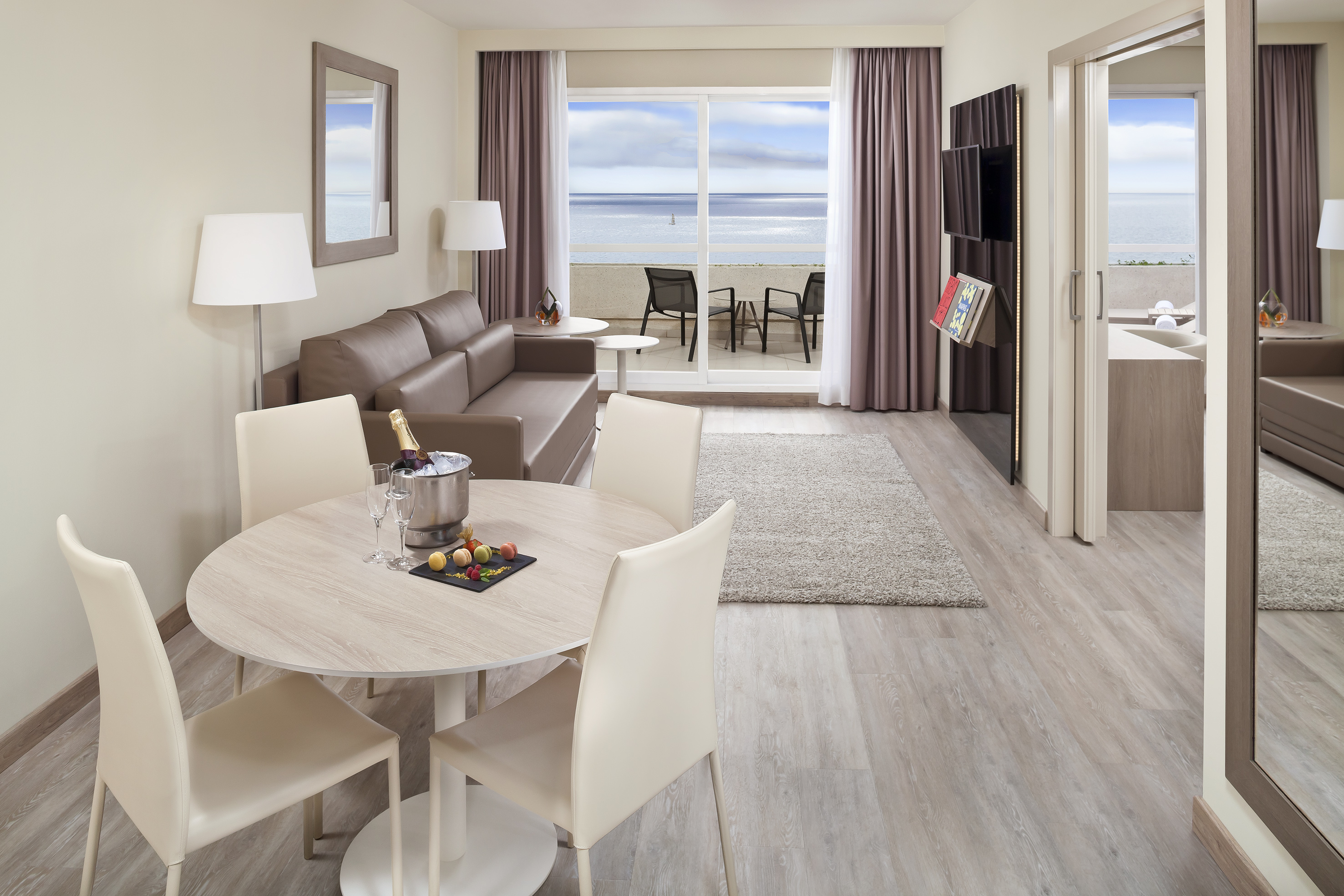 Modern hotel suite with ocean view, living area, dining table, balcony.