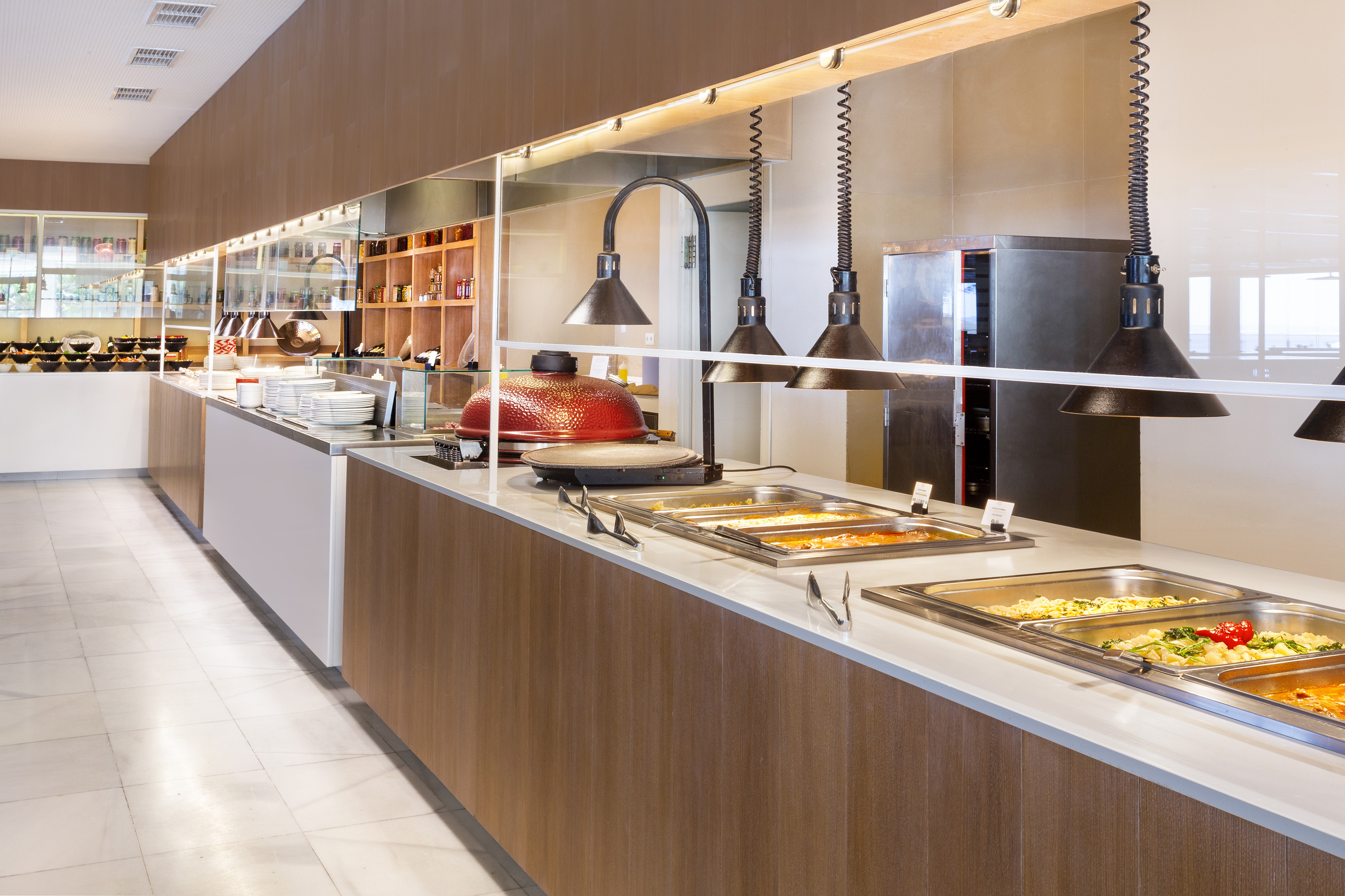 Modern hotel buffet with hot food warming trays and a red kamado grill.