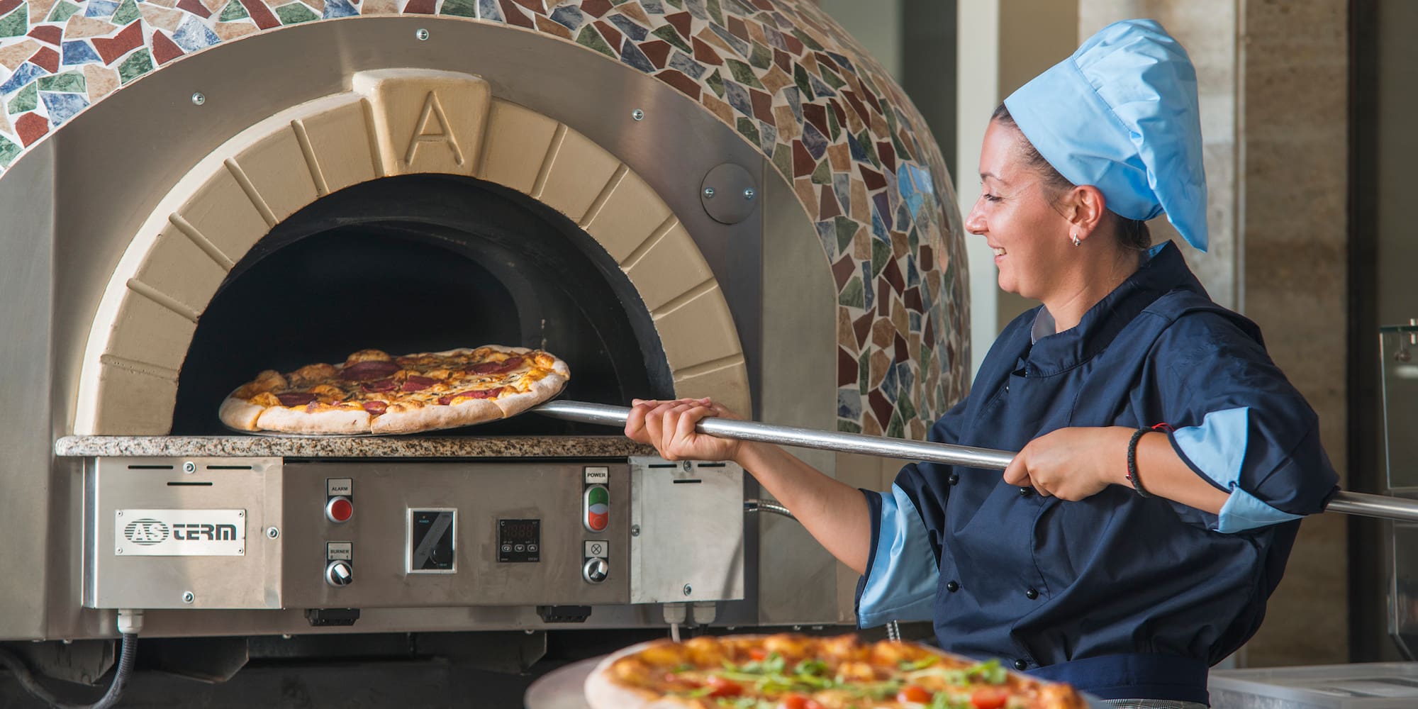 a woman in chef hat cooking pizza in a oven