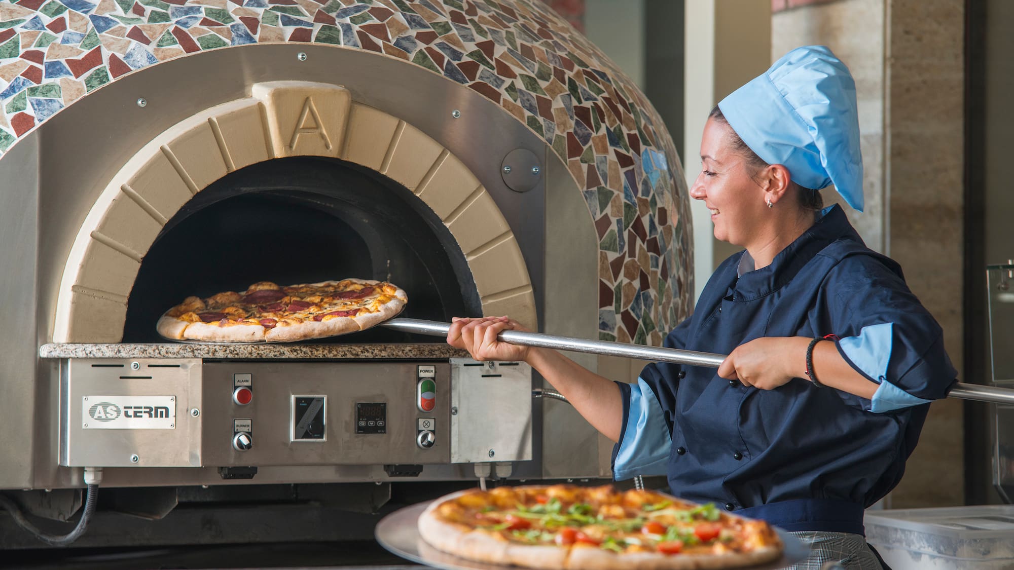 a woman in chef hat cooking pizza in a oven