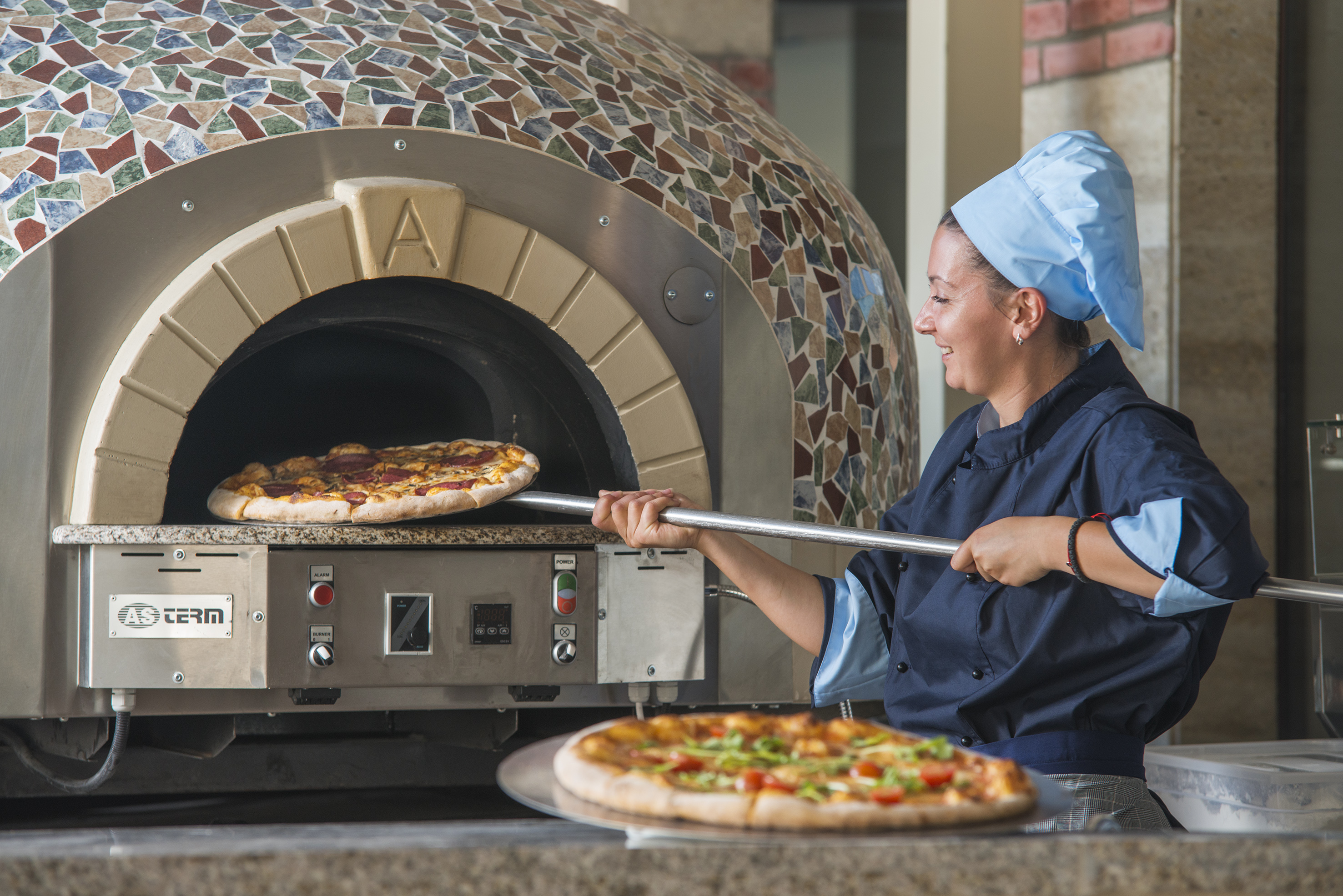 a woman in chef hat cooking pizza in a oven