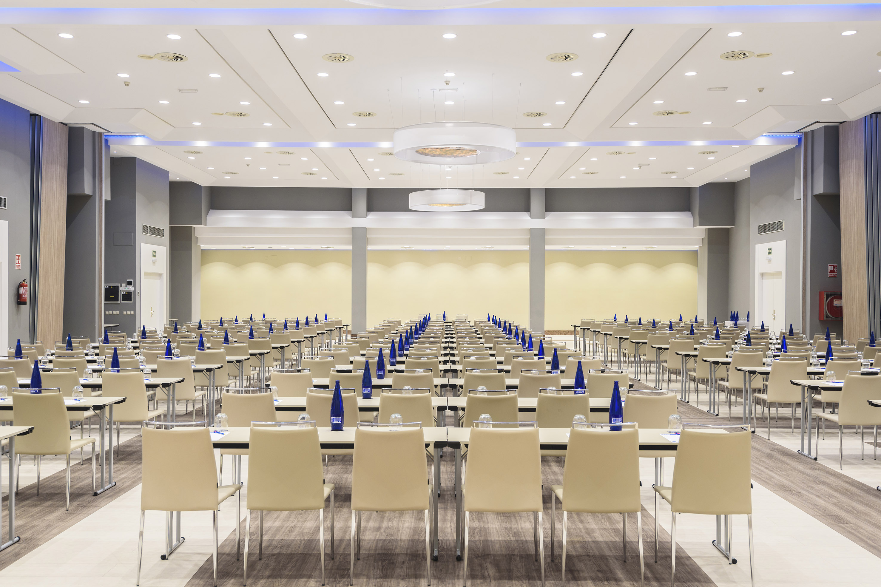 Modern conference room with many tables, beige chairs, and blue water bottles.