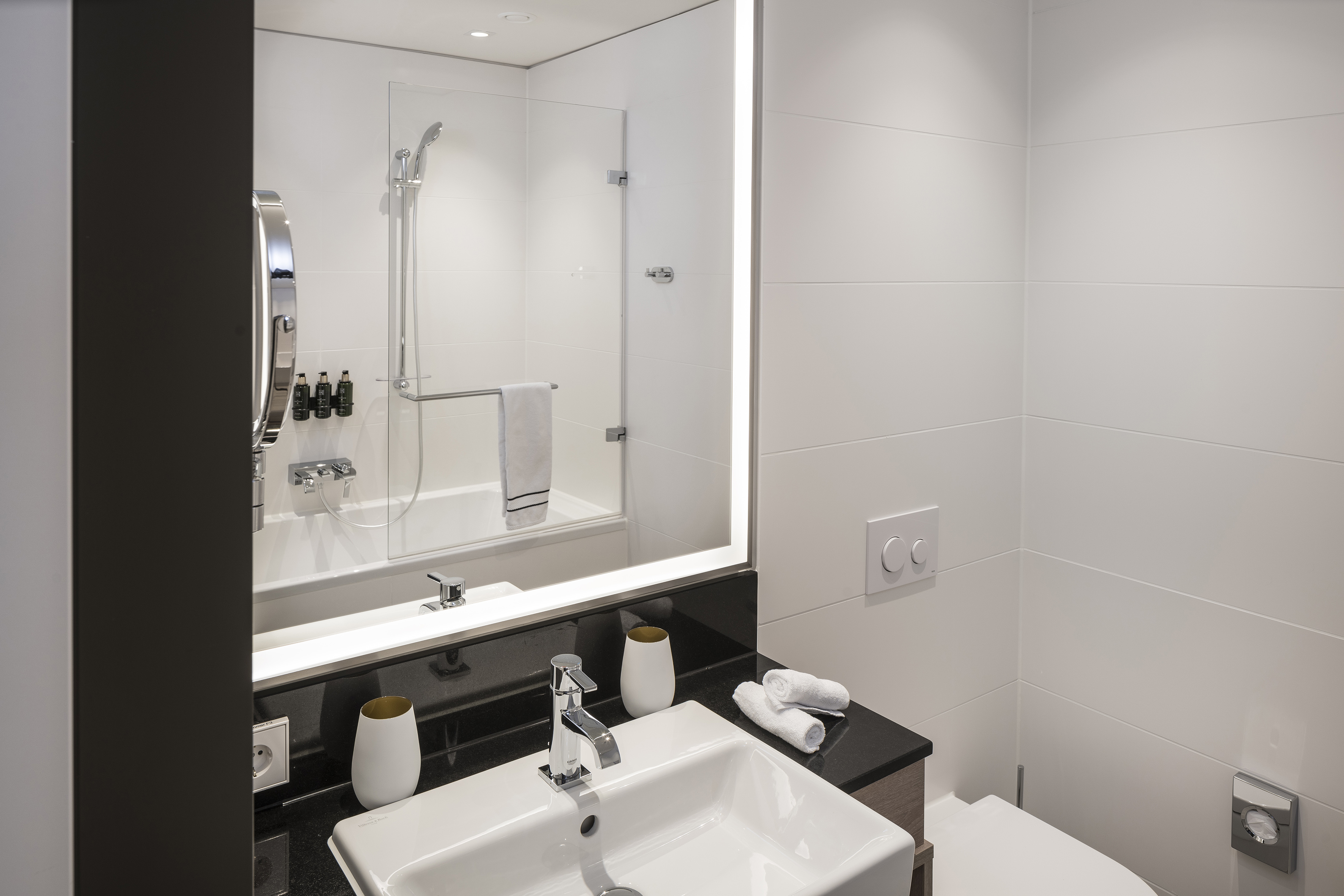 Modern bathroom with white tiled walls, vanity sink, and illuminated mirror.