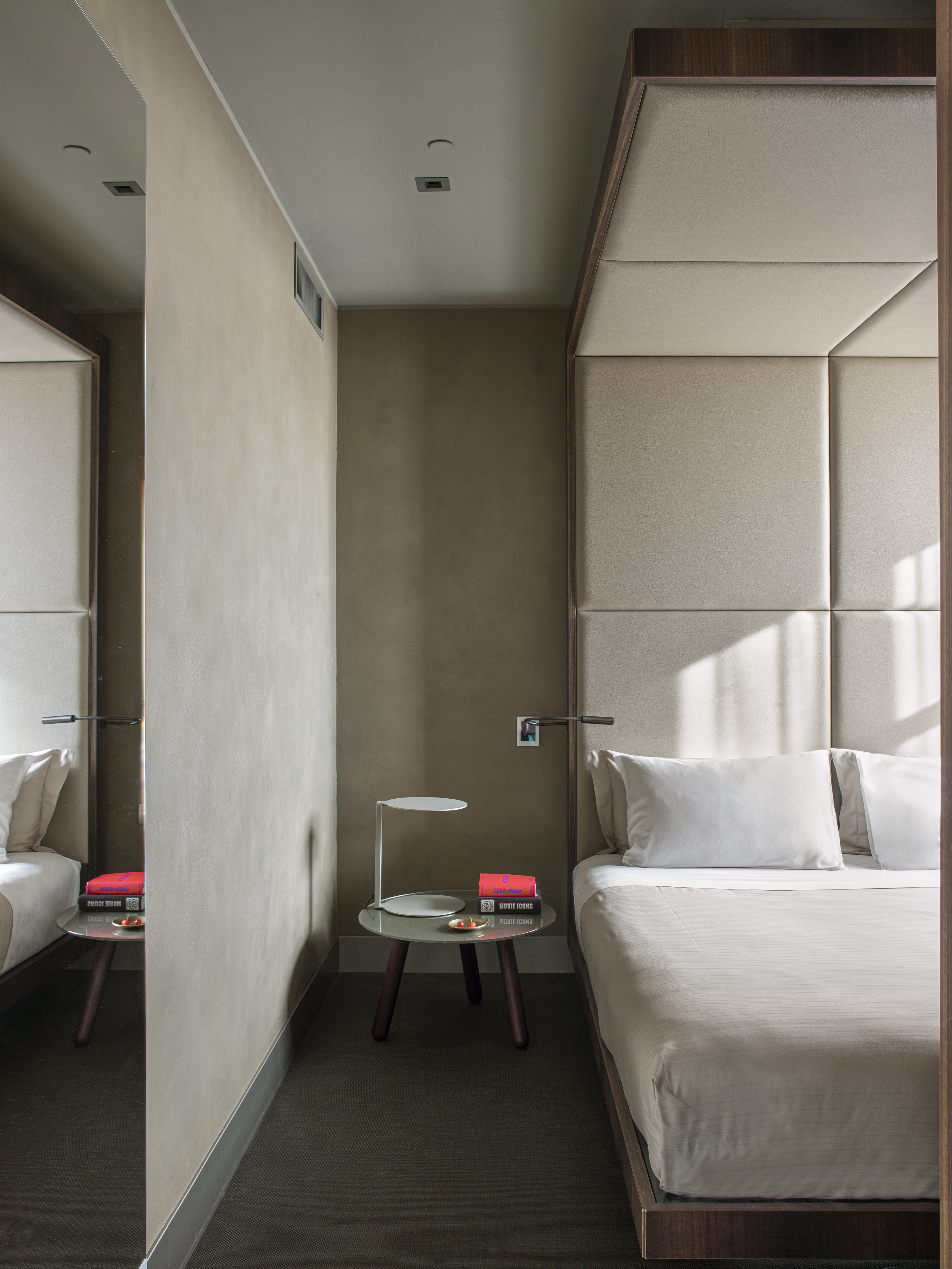 Hotel bedroom with padded headboard, dark wood bed, and minimalist nightstand.