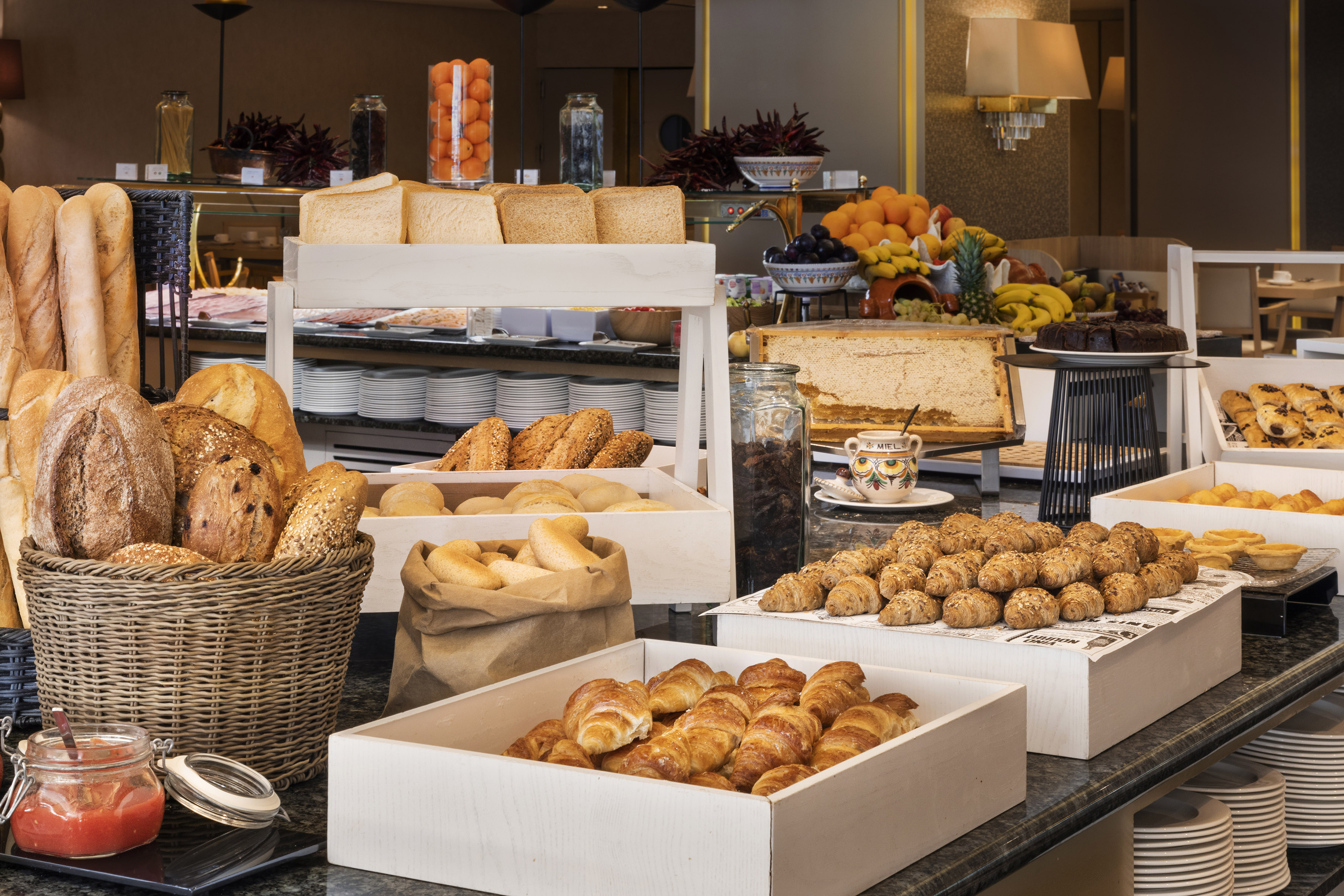 Hotel breakfast buffet with fresh breads, croissants, pastries, and abundant fruits.