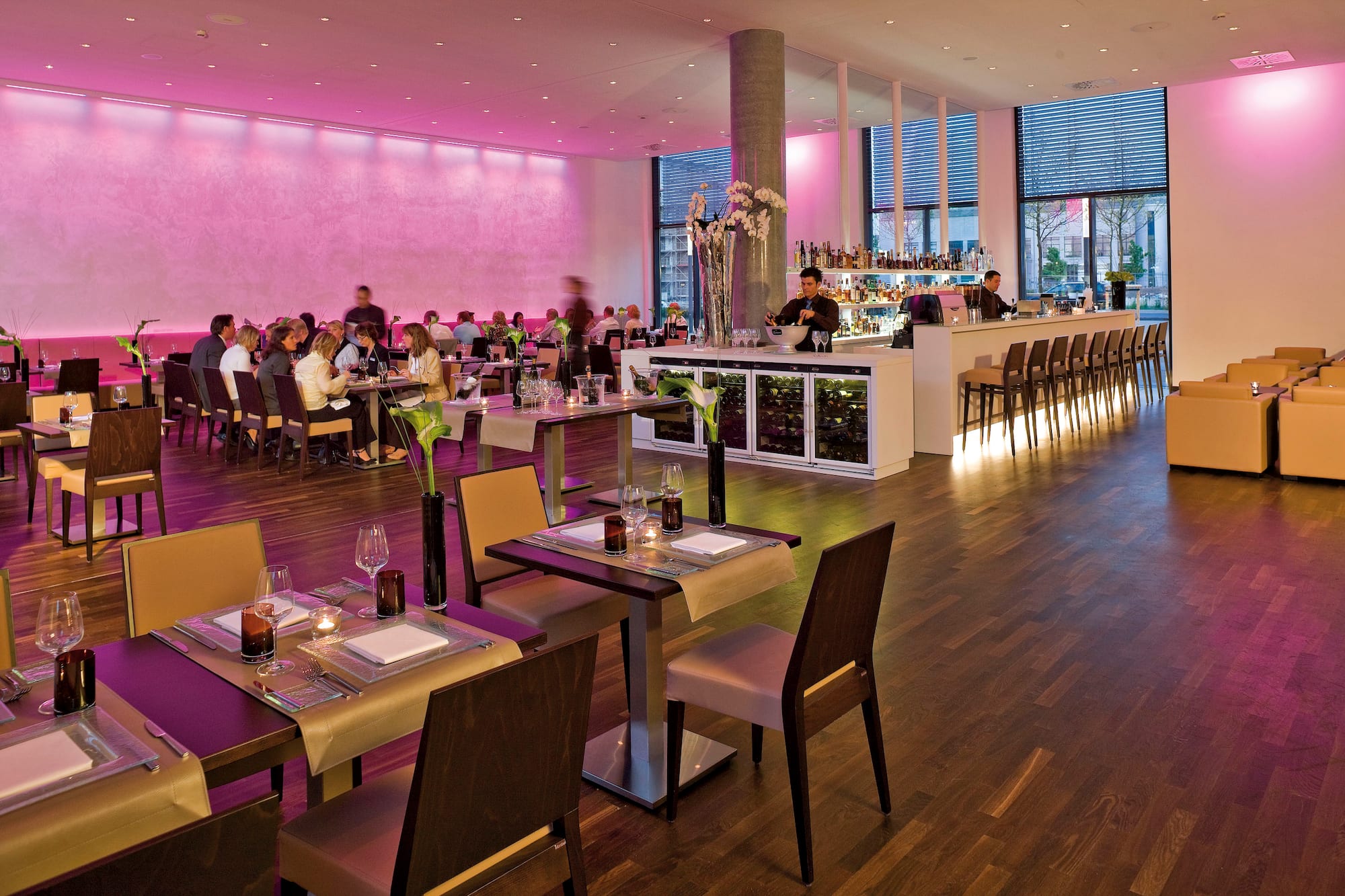 Modern restaurant and bar with guests, pink ambient lighting, and wooden floors.