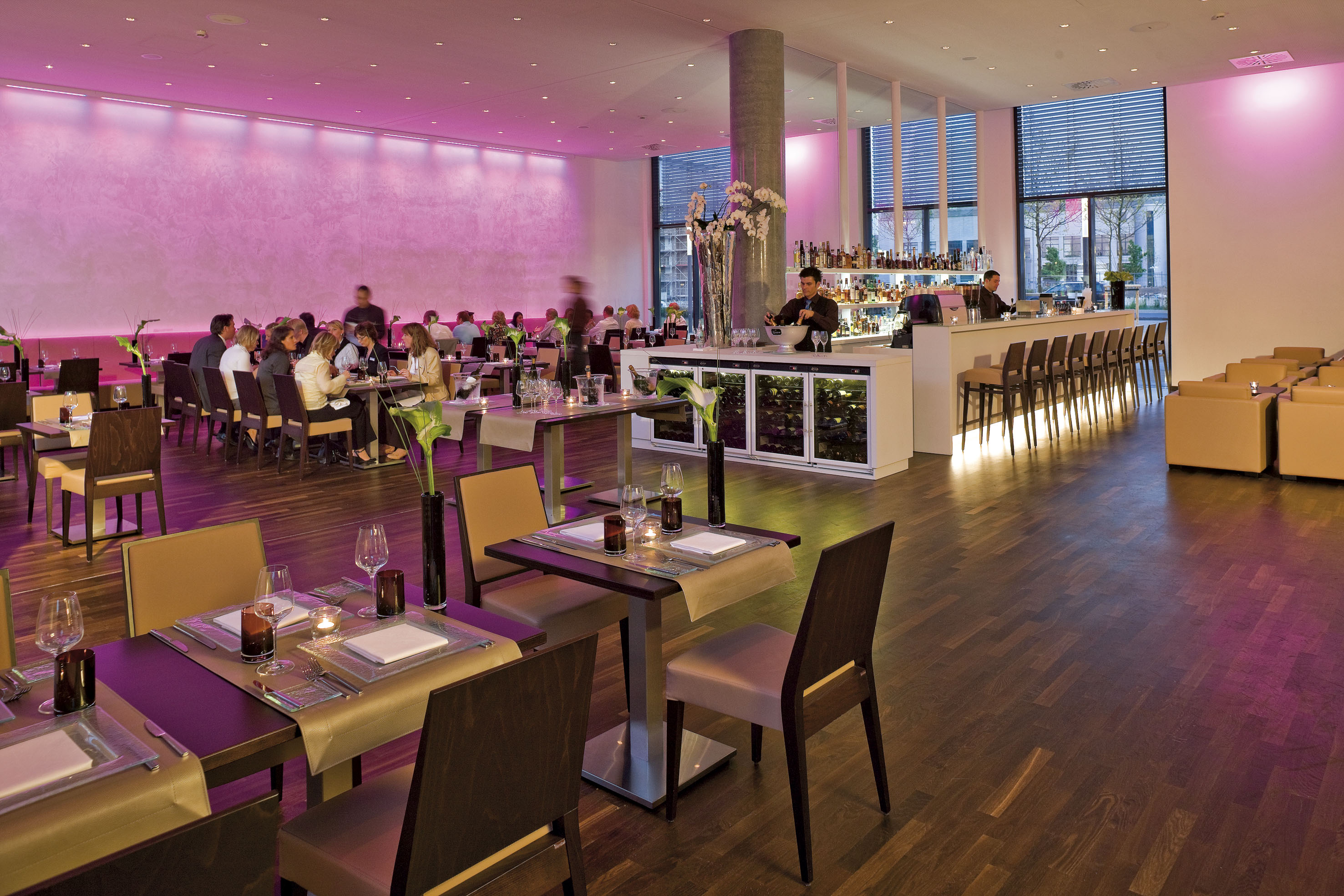 Modern restaurant and bar with guests, pink ambient lighting, and wooden floors.