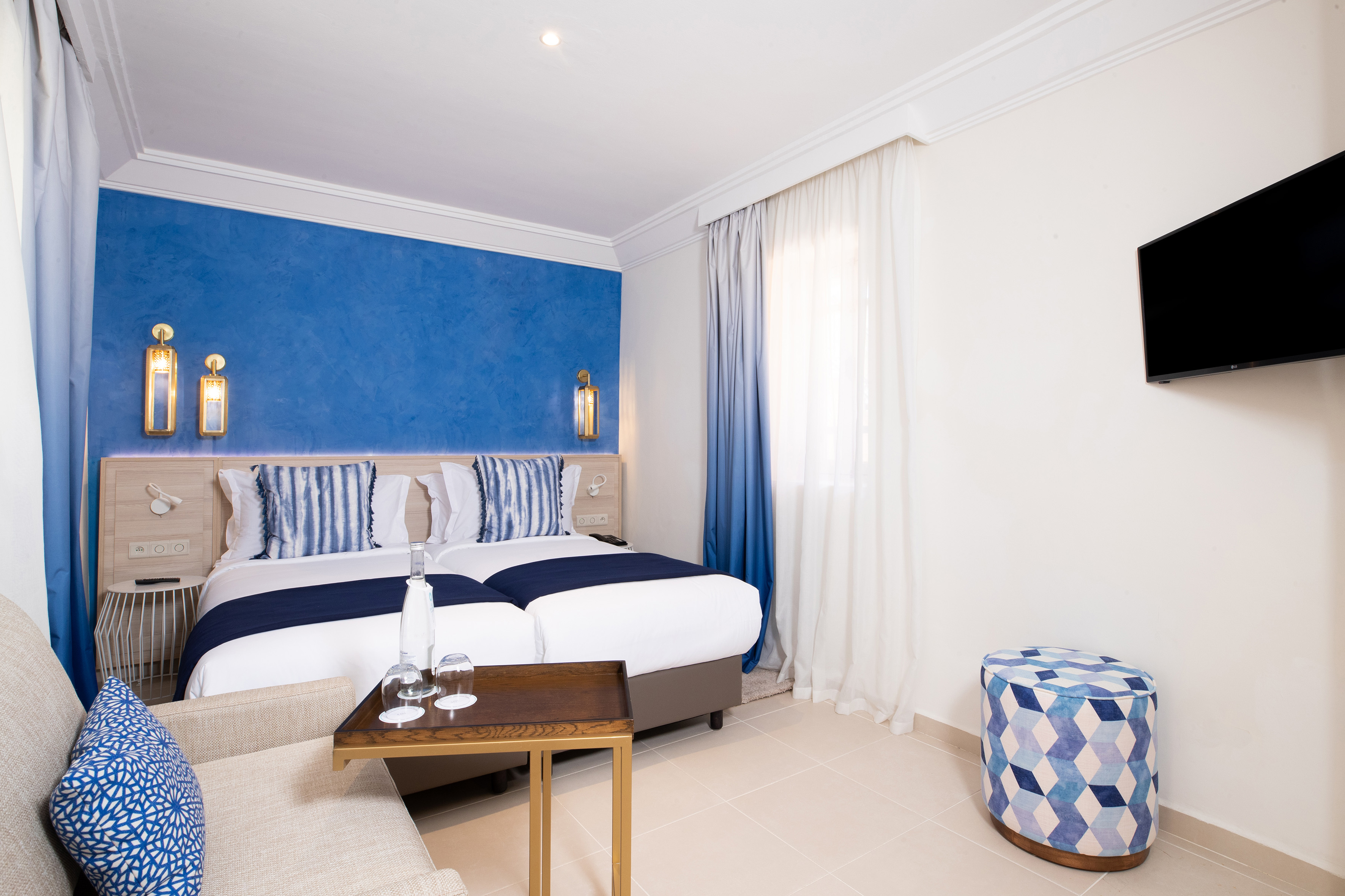 Comfortable hotel bedroom with twin beds, blue accent wall, and modern decor.