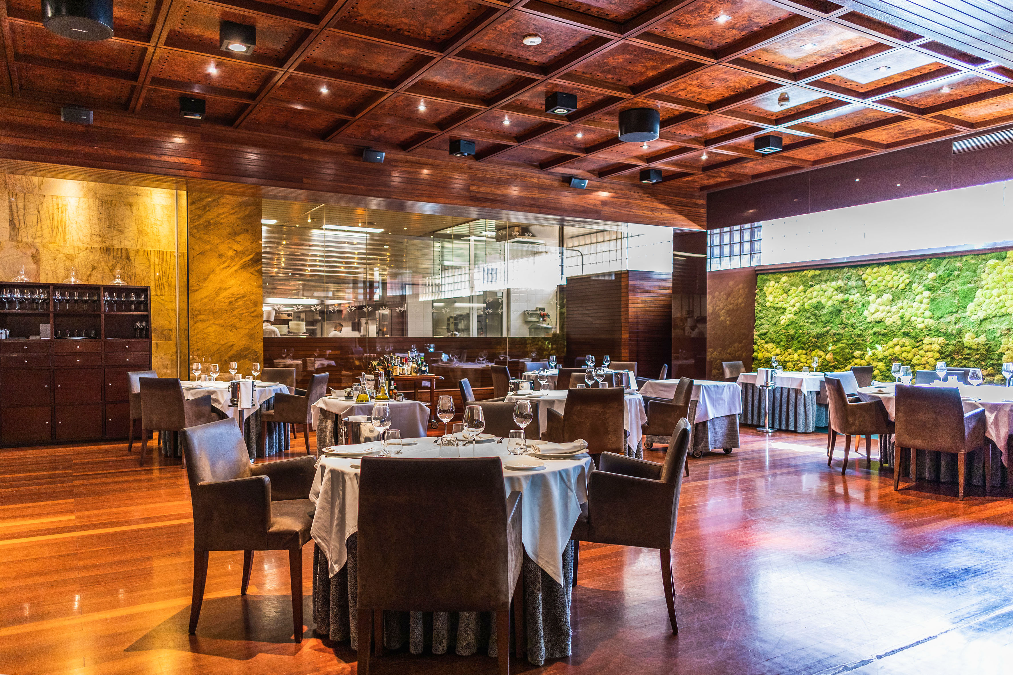 Fine dining restaurant interior with polished wood, set tables, and a vibrant green wall.