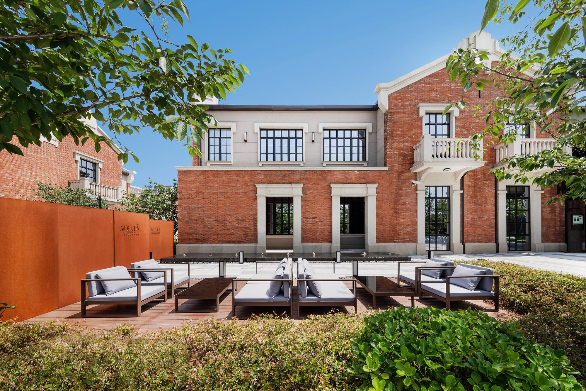 Melia red brick building exterior with modern outdoor lounge and green plants.