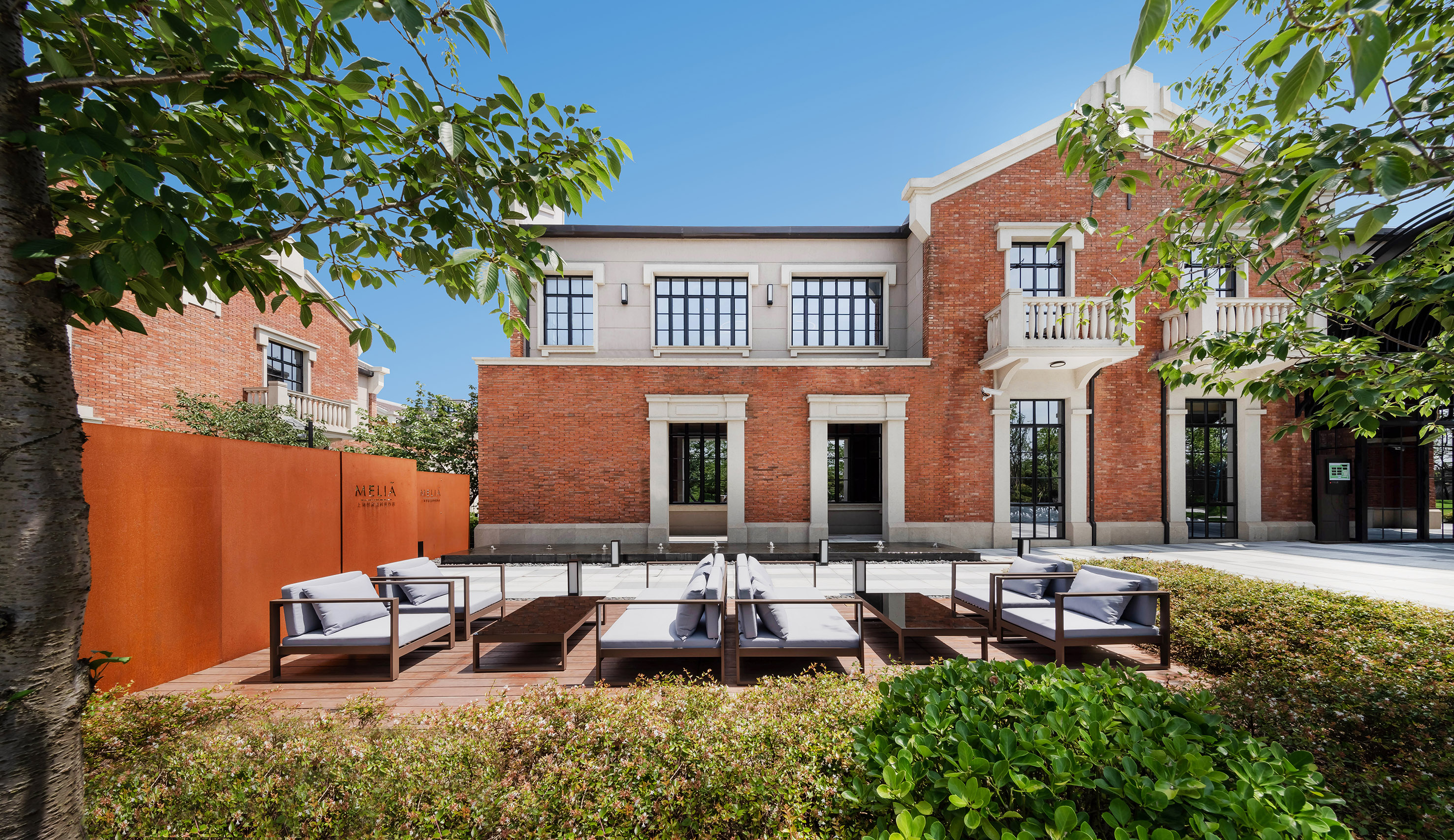 Melia red brick building exterior with modern outdoor lounge and green plants.