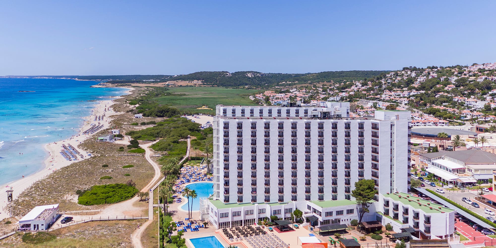 a large white building with a pool and a beach in the background