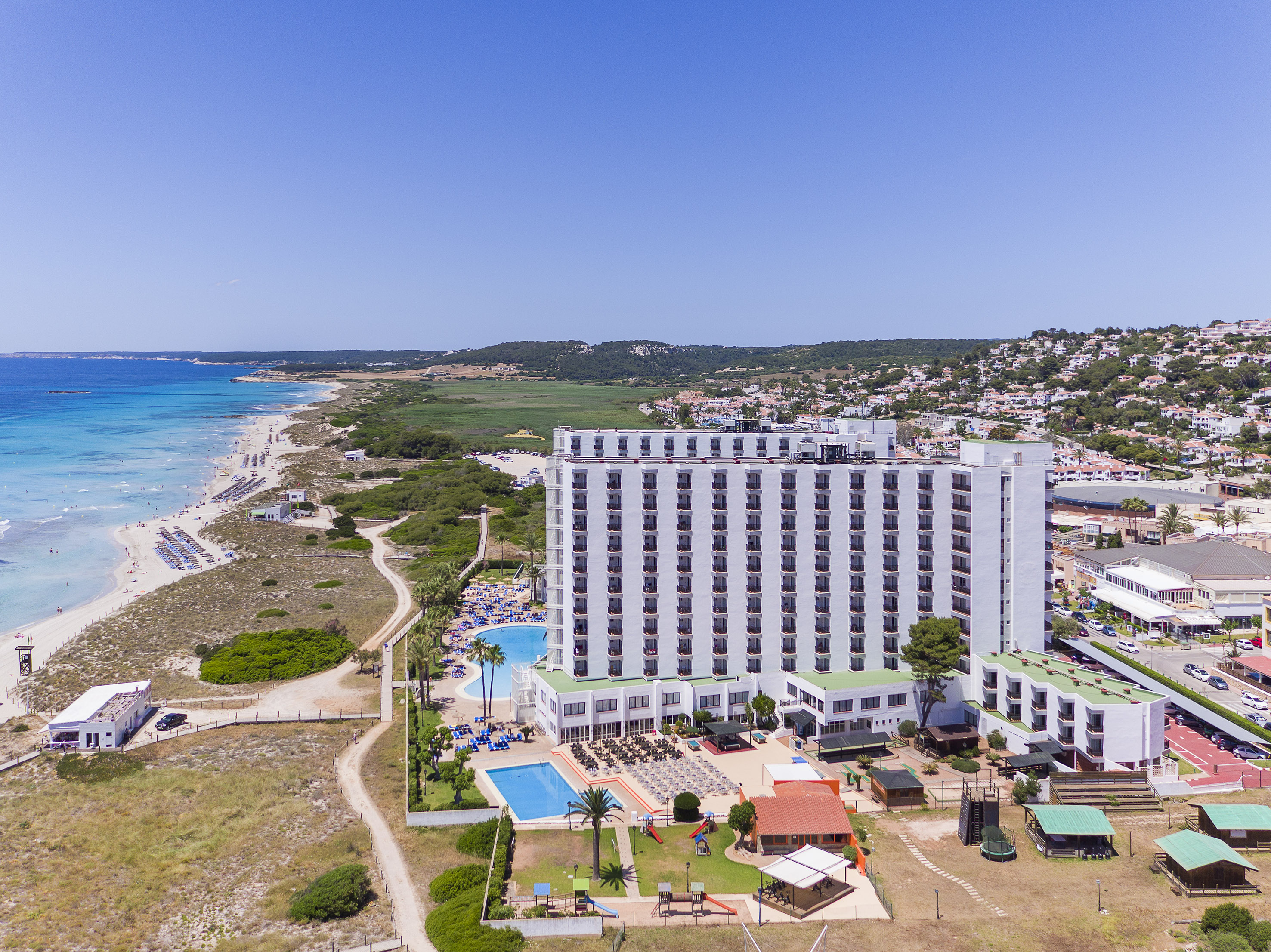 a large white building with a pool and a beach in the background