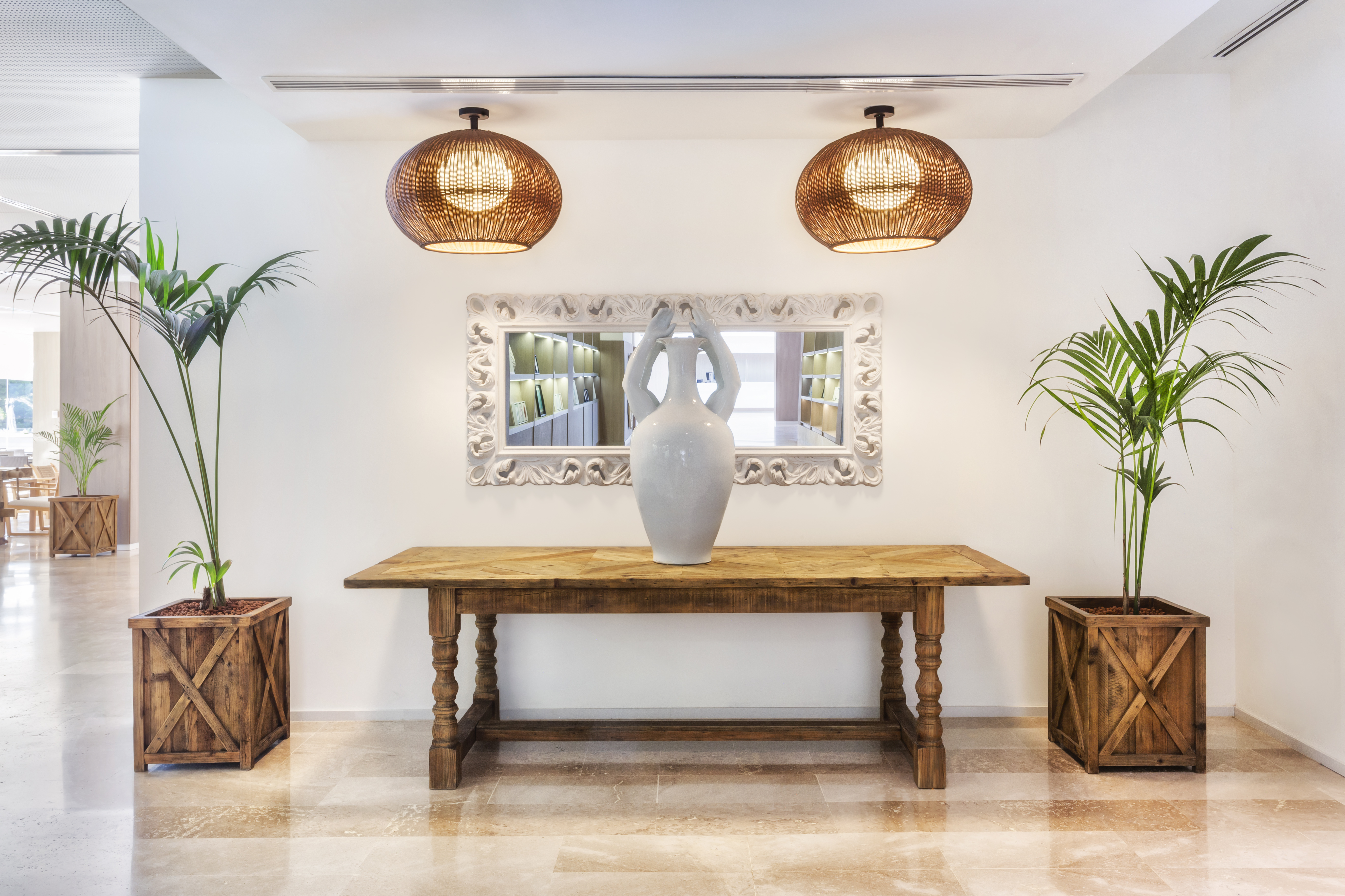 Lobby decor: wooden console table, ornate mirror, white vase, and palm plants.