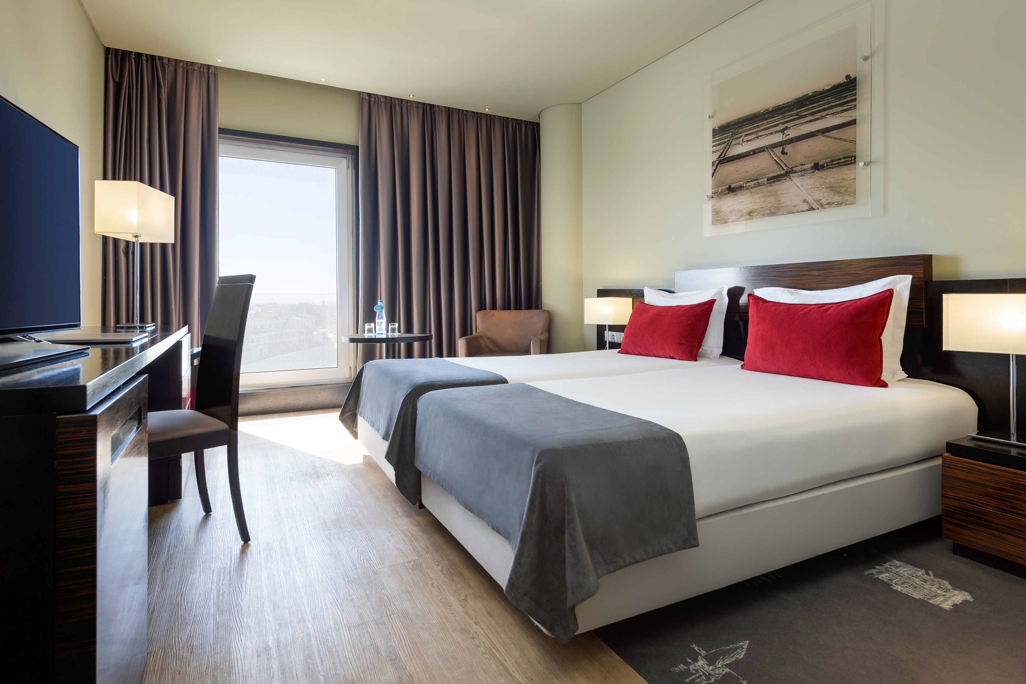 Bright hotel twin room with modern decor, red accents, desk, and window view.