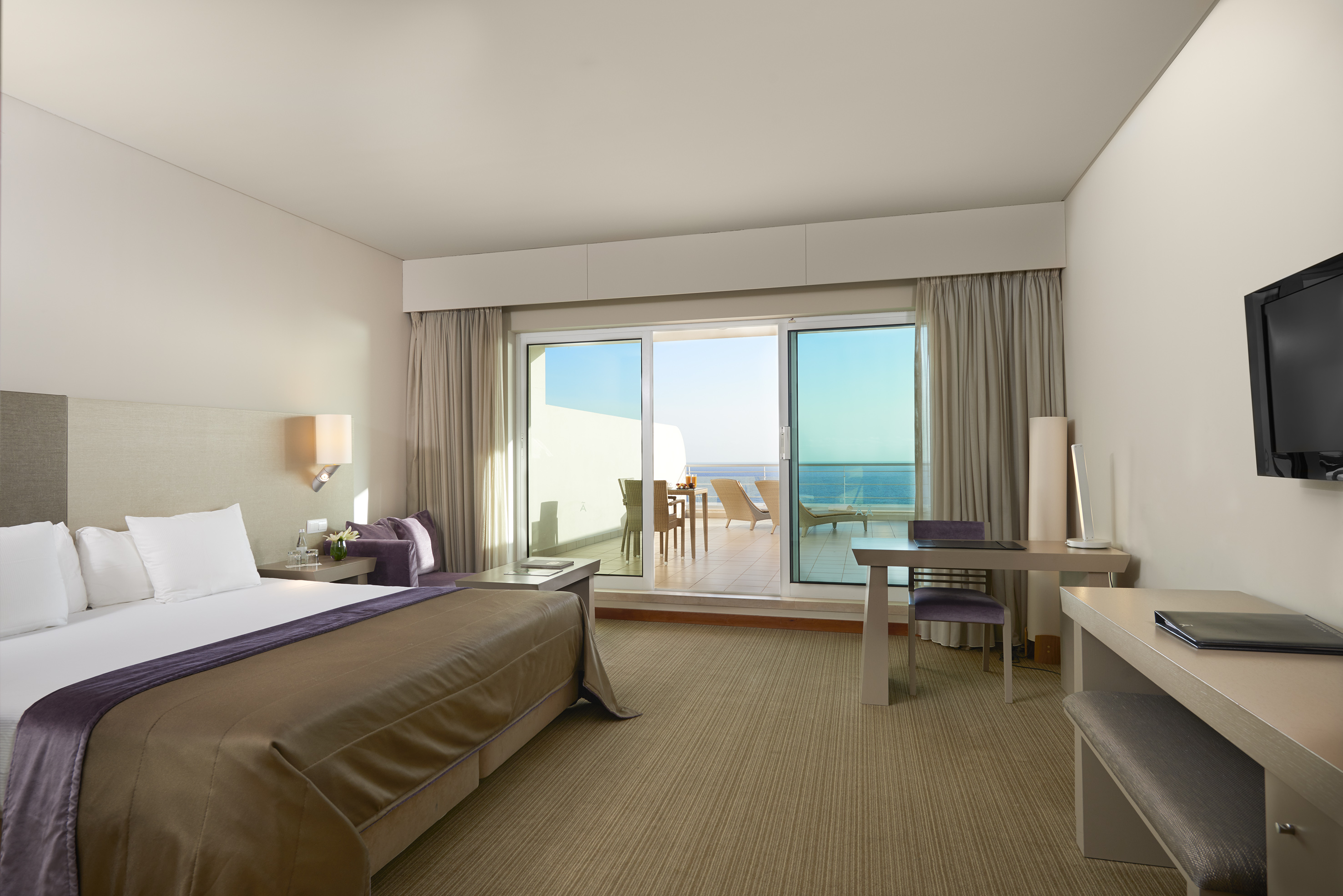 Hotel room with ocean view balcony, large bed, and work desk.
