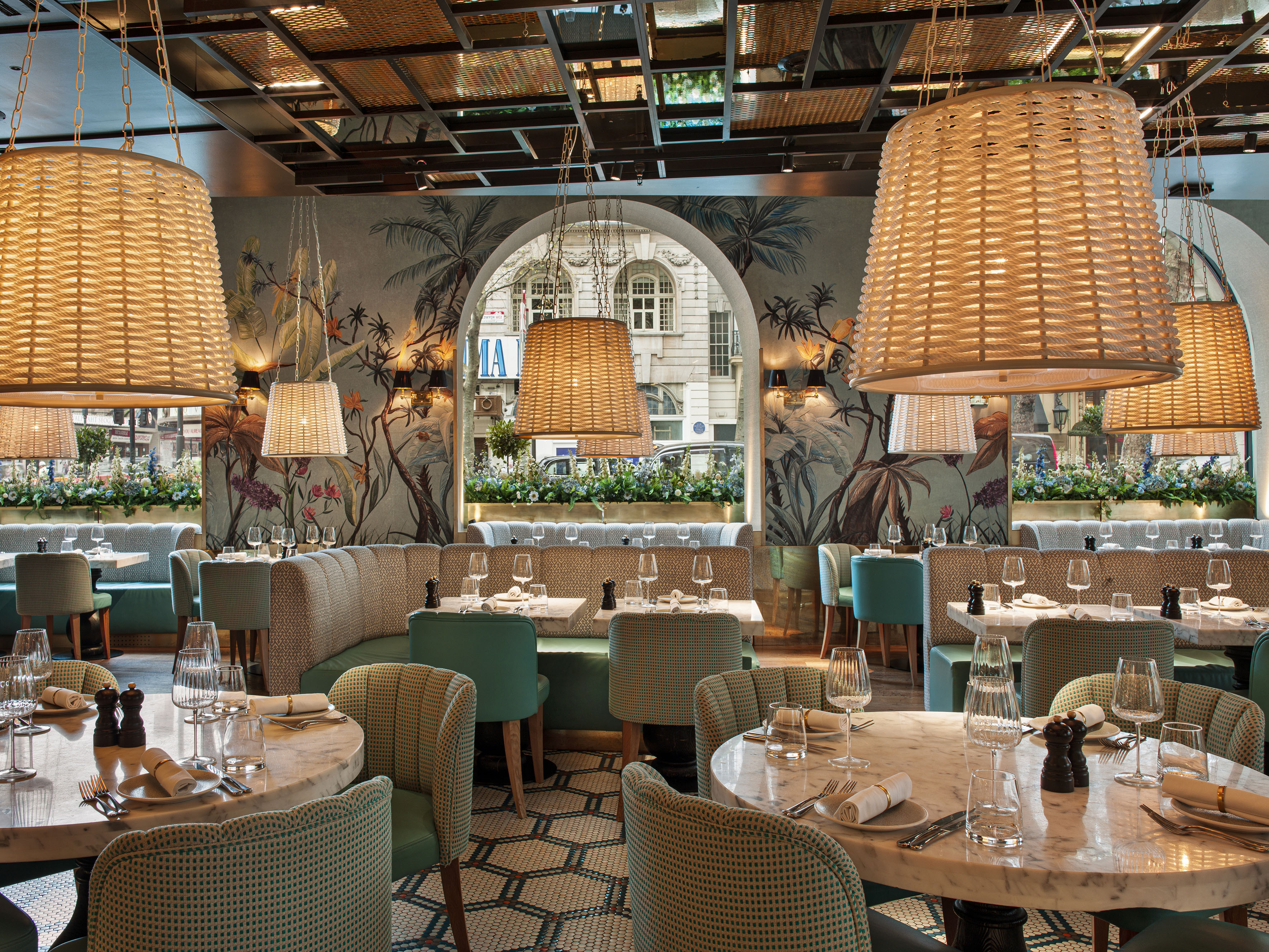 Tropical-themed restaurant interior with wicker lamps, marble tables, and green seating.
