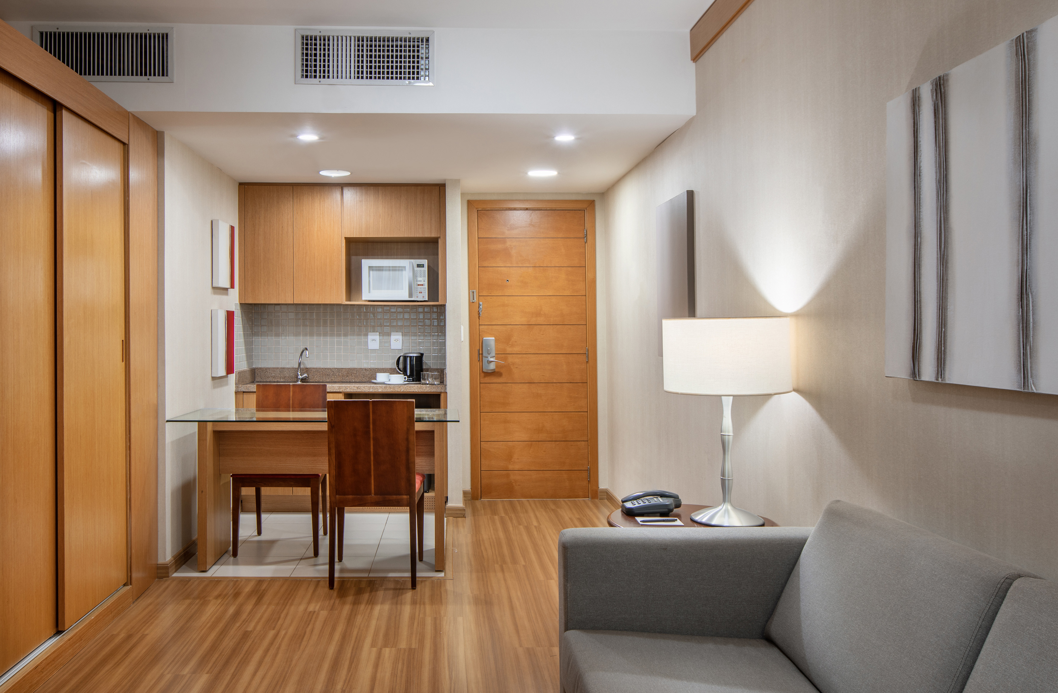 Hotel suite interior with kitchenette, dining table, and living area with sofa.